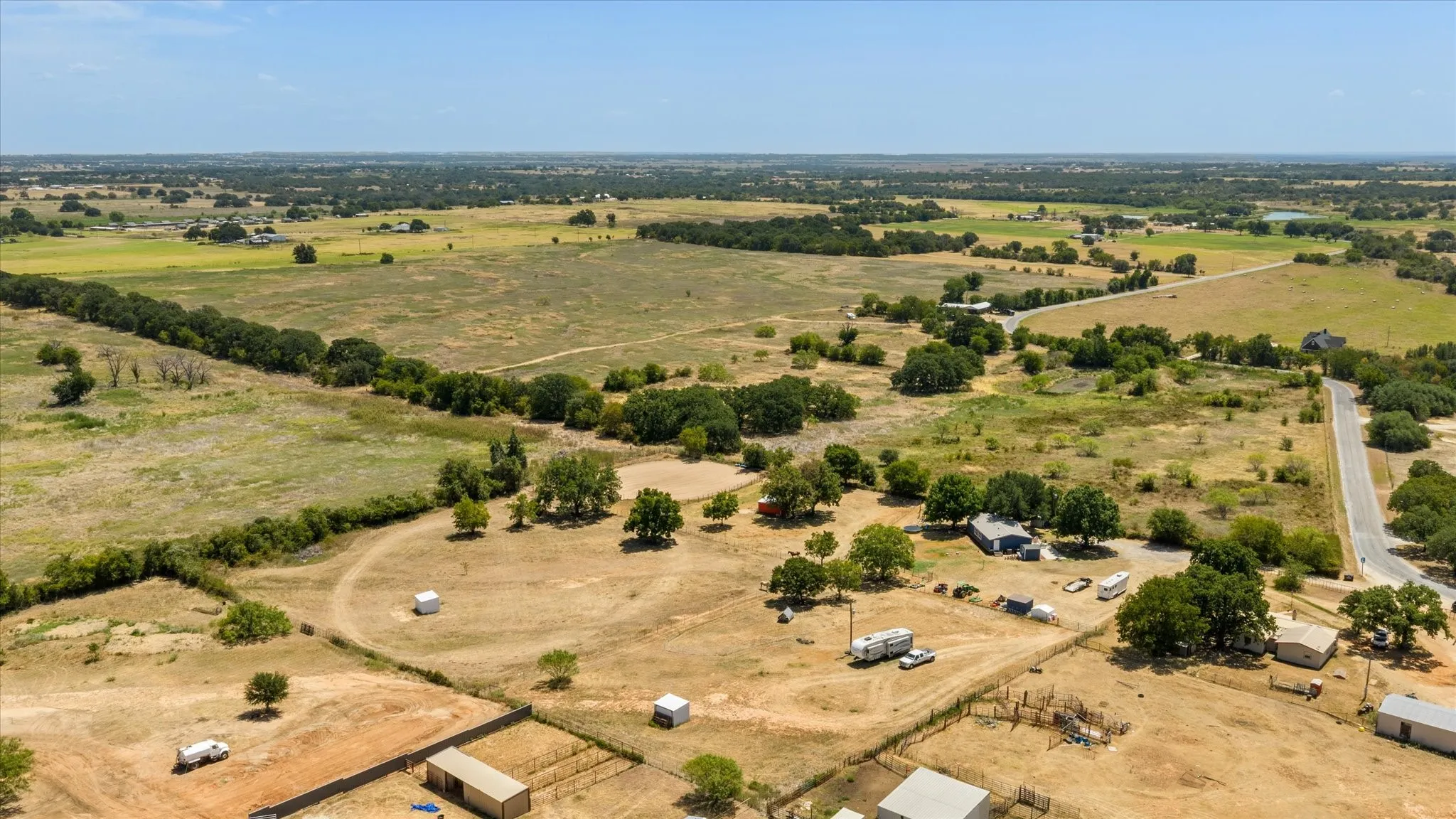 Expansive rural landscape and privacy, featuring scattered mature trees, open fields, a paved road, and a residential structure