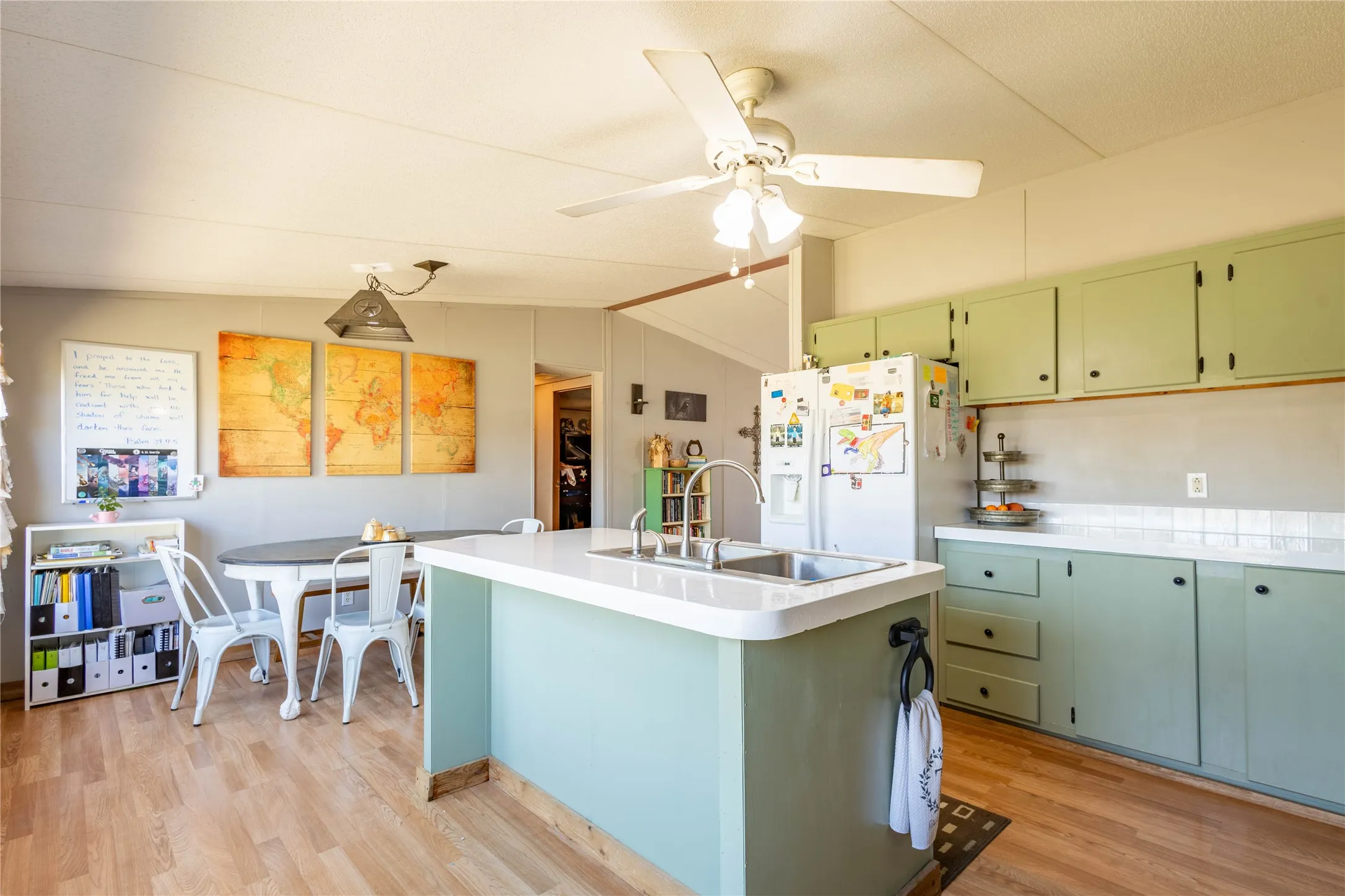 Kitchen with wood-finish flooring, an island with an integrated sink, sage green cabinetry, and white countertops