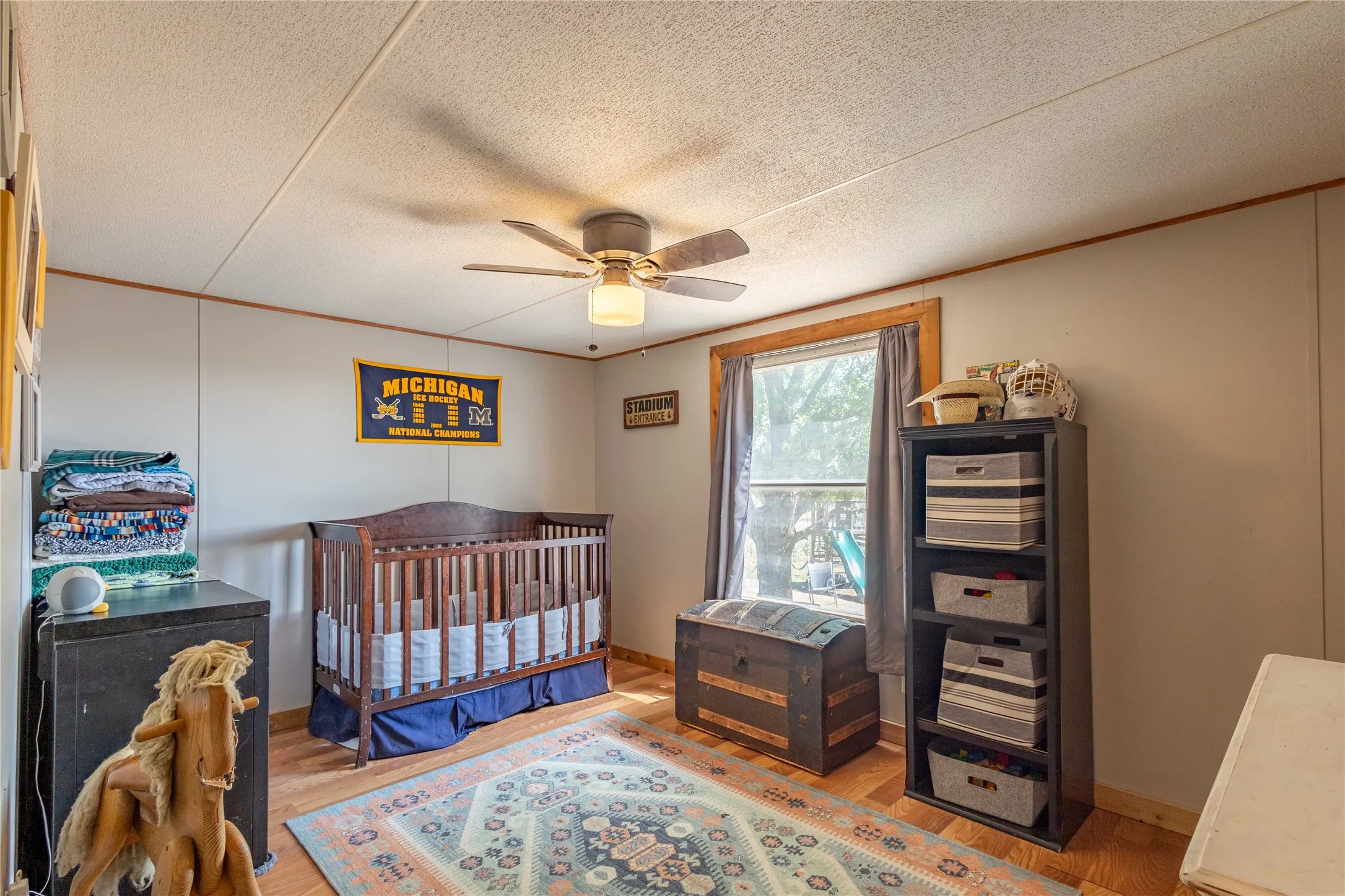 Wood-finish flooring, a window with wood trim, and a ceiling fan with integrated lighting