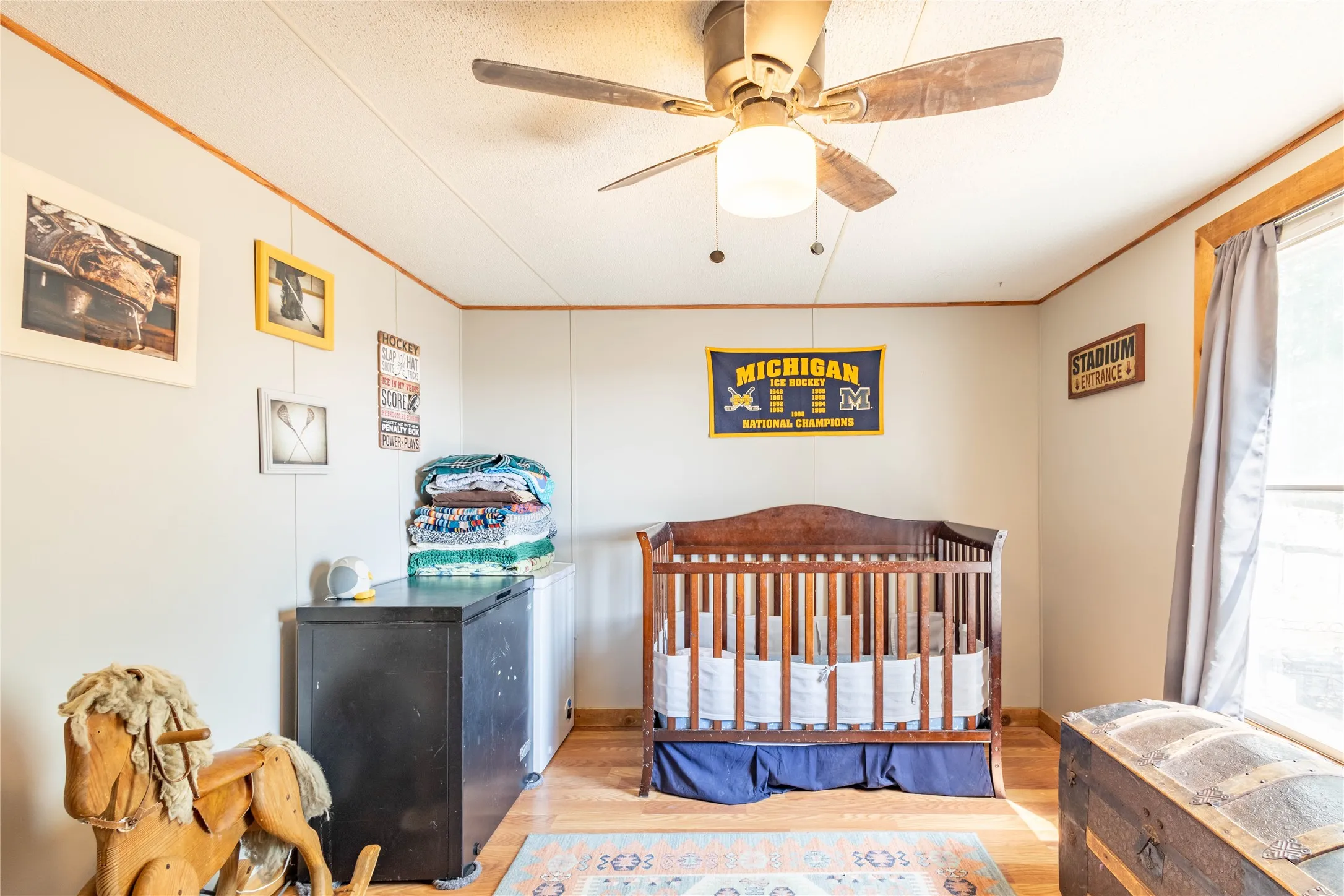 Wood-finish flooring, ceiling fan with integrated lighting, natural wood trim, and a window providing natural light
