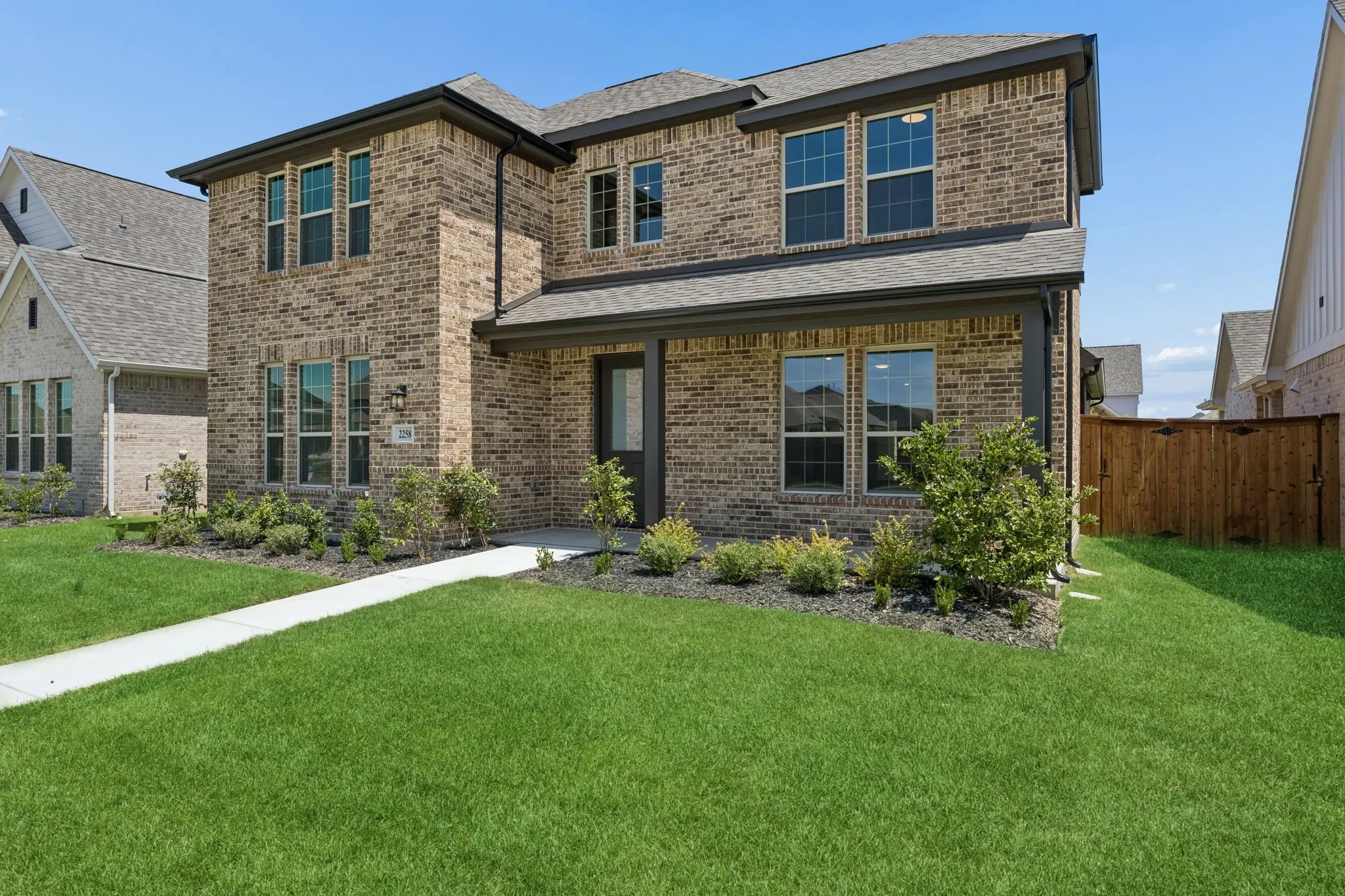 Two-story brick exterior, covered front entry, dark trim accents, multiple windows, and a landscaped front yard