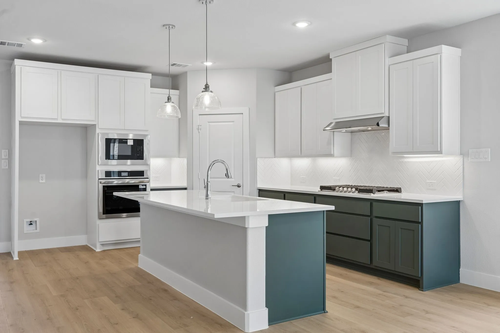 Contemporary kitchen featuring wood-finish flooring, a central island with a white countertop, two-tone cabinetry, stainless steel appliances, and pendant lighting