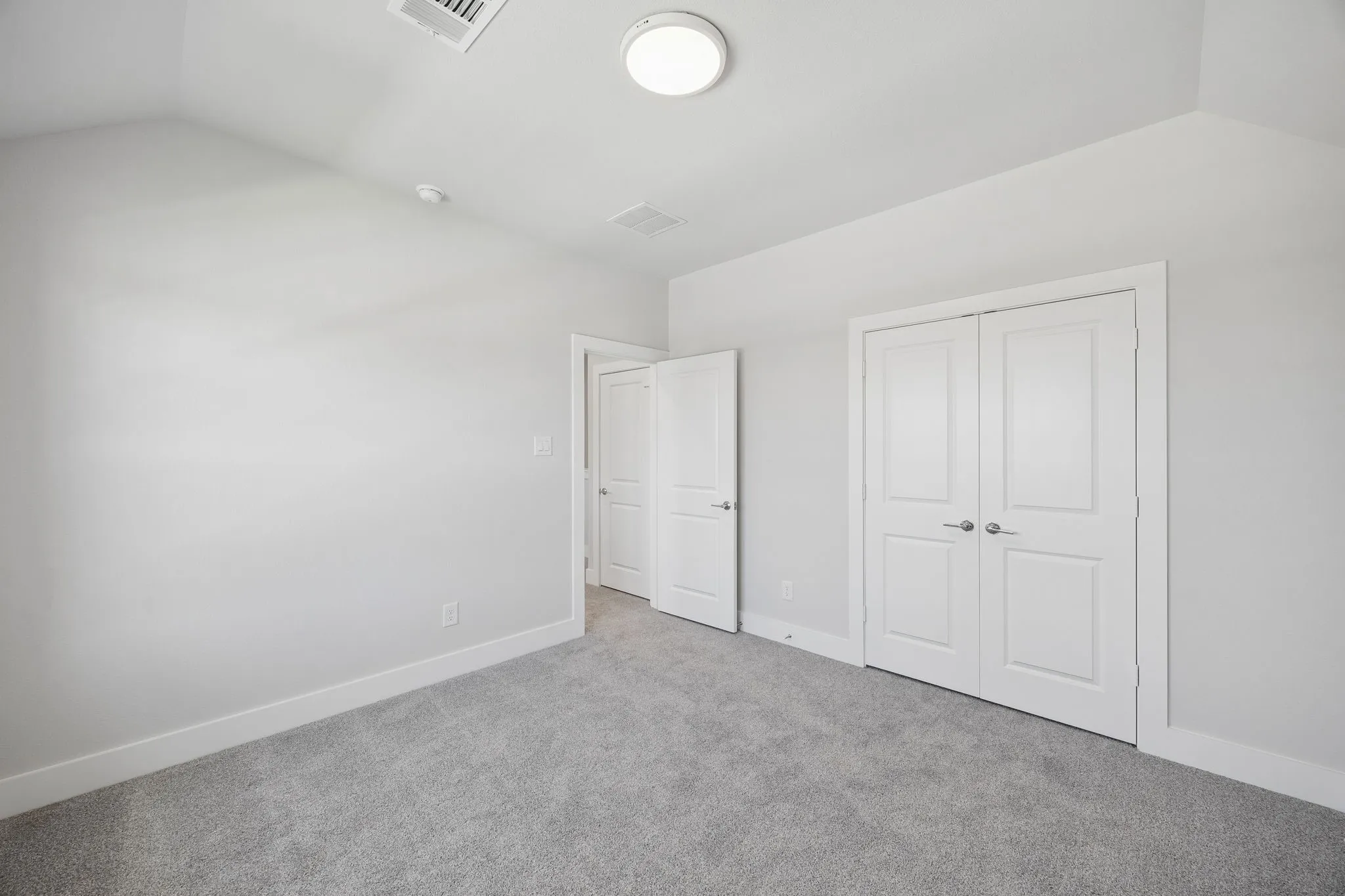 Vaulted ceiling, recessed lighting, flush mount lighting, gray wall paint, gray carpeting, bi-fold panel doors