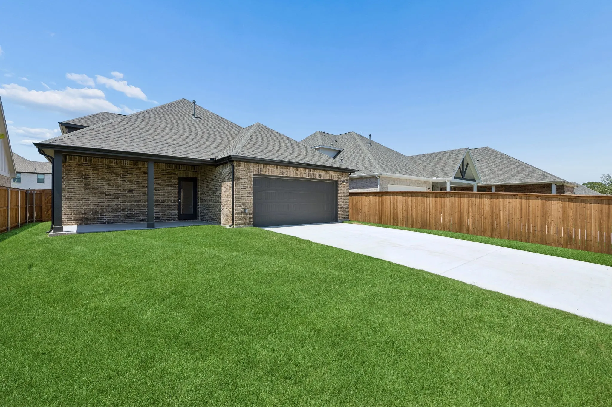 Brick exterior with covered patio, attached garage, concrete driveway, and wood privacy fencing
