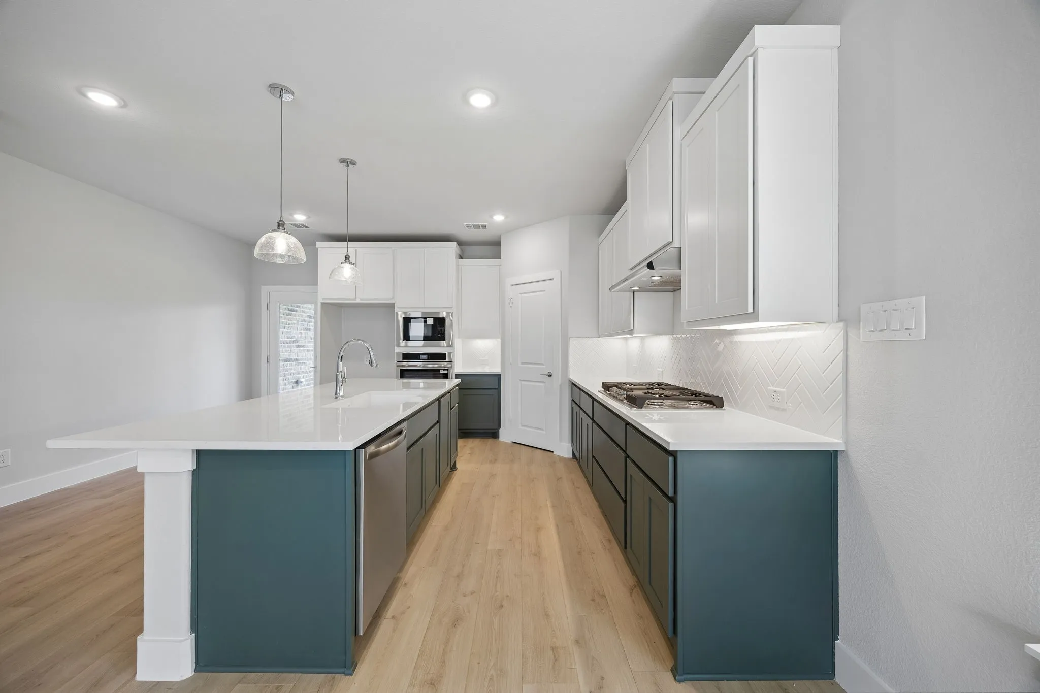 Central kitchen island with sink and pendant lighting, stainless steel appliances, herringbone tile backsplash, wood-finish flooring, and white upper cabinetry