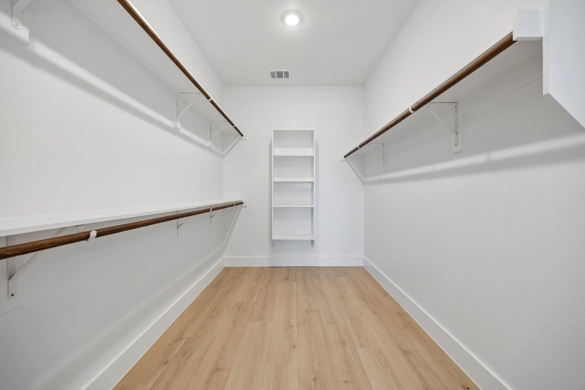 Spacious walk-in closet featuring wood-finish flooring, white shelving, and dual clothing rods