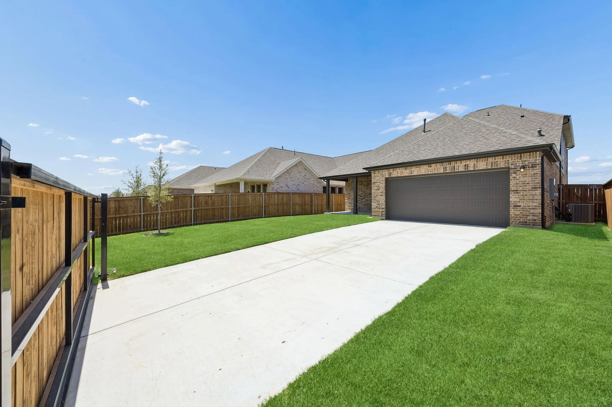 Brick exterior featuring a two-car garage, concrete driveway, and a wood privacy fence