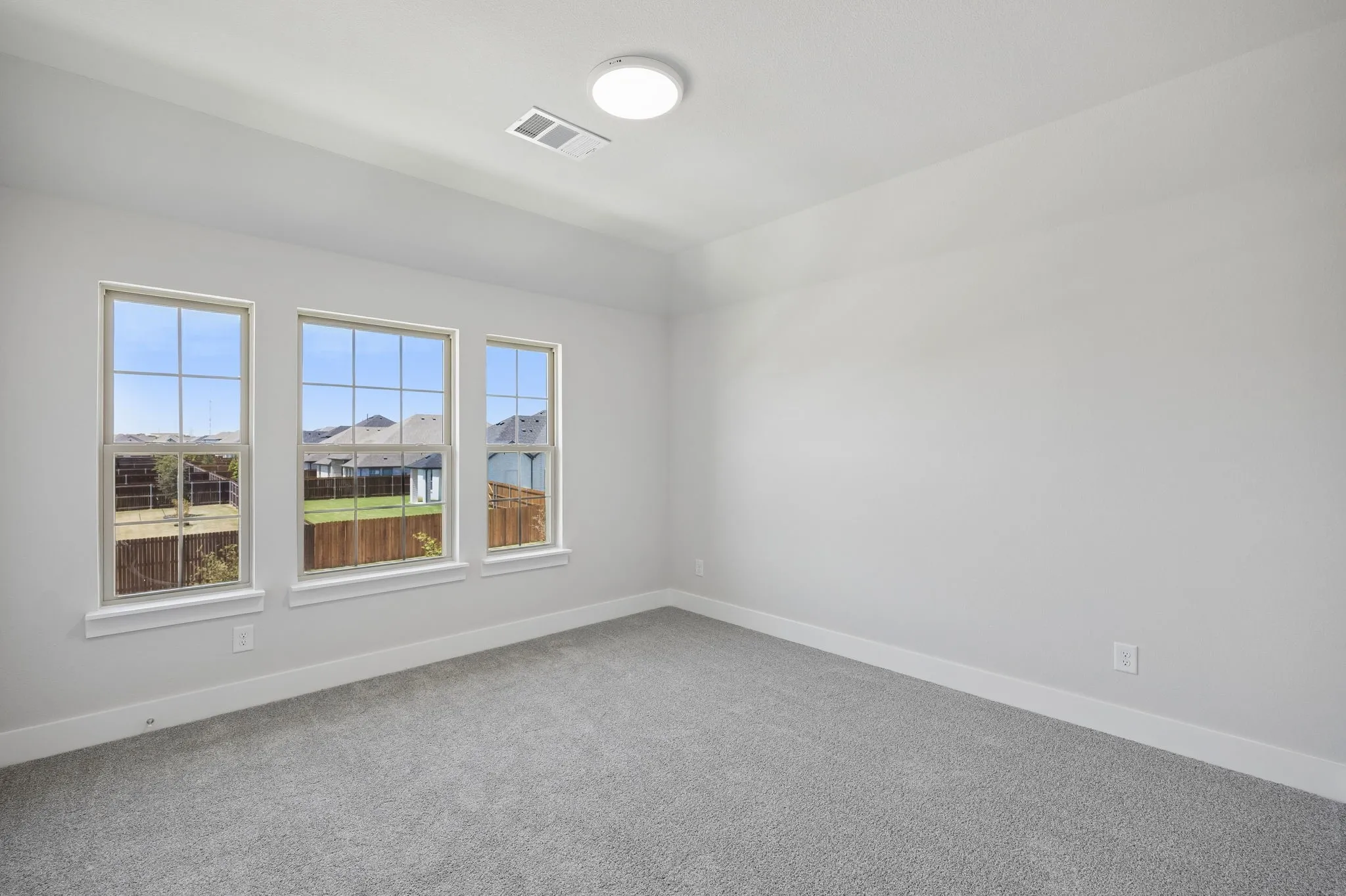 Neutral gray wall finish, plush gray carpeting, three gridded windows, white window trim, and a flush-mount ceiling light