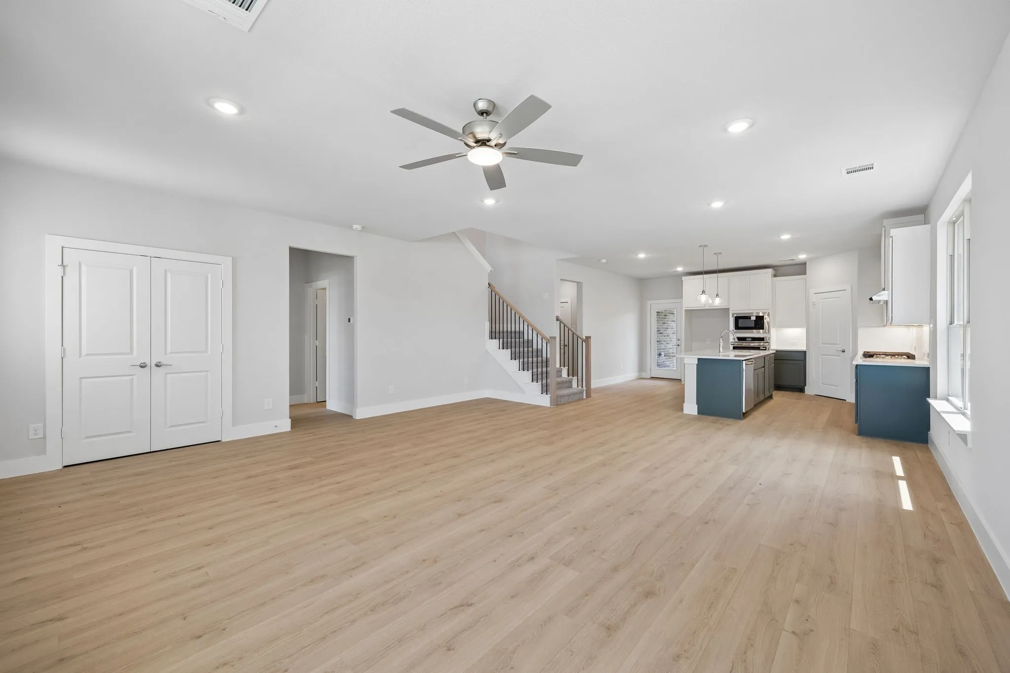 Open-concept living area featuring wood-finish flooring, recessed lighting, a modern ceiling fan, and a kitchen with an island and white cabinetry