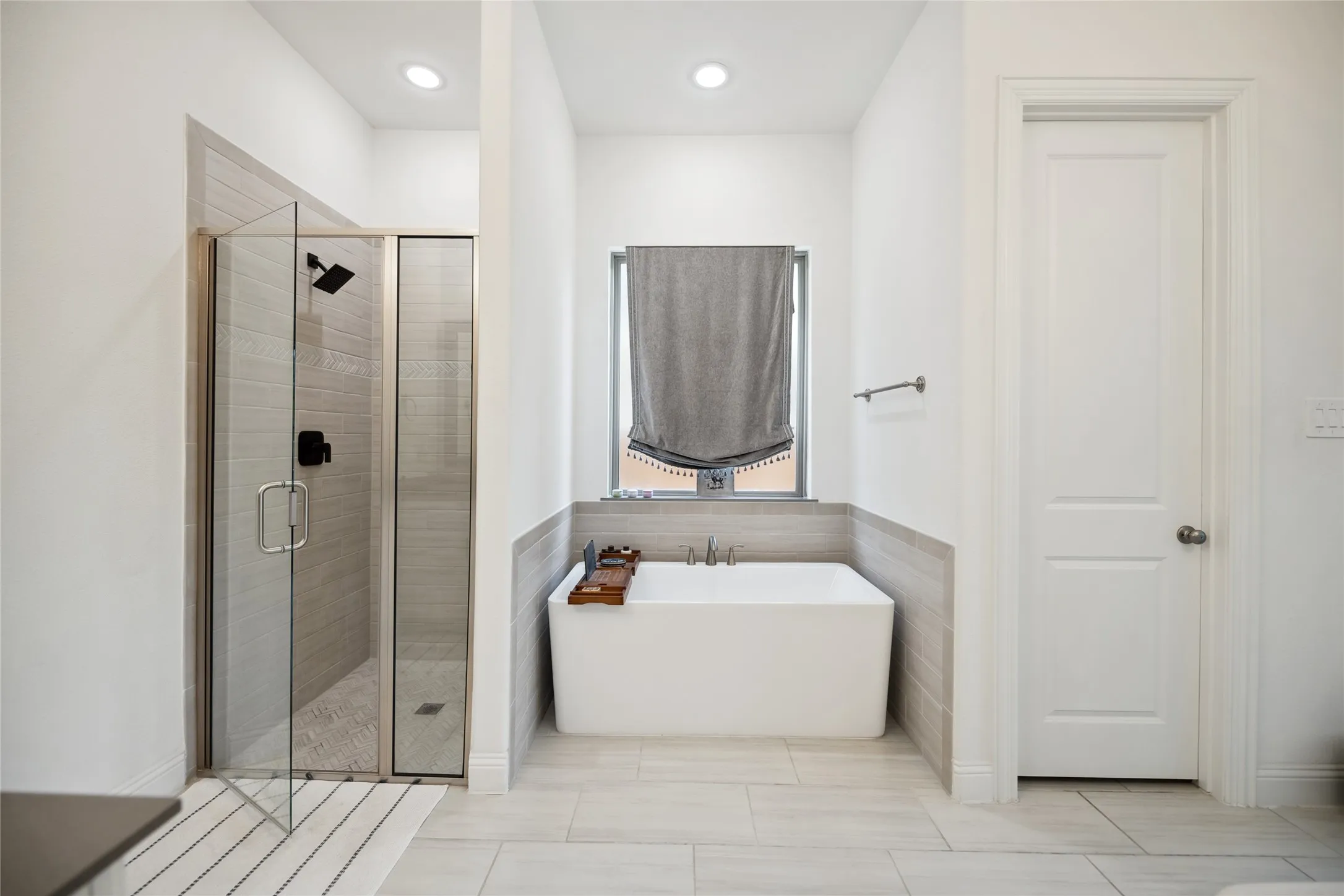 Spacious bathroom featuring a freestanding tub, glass-enclosed shower with a matte black fixture, and light-toned tile flooring