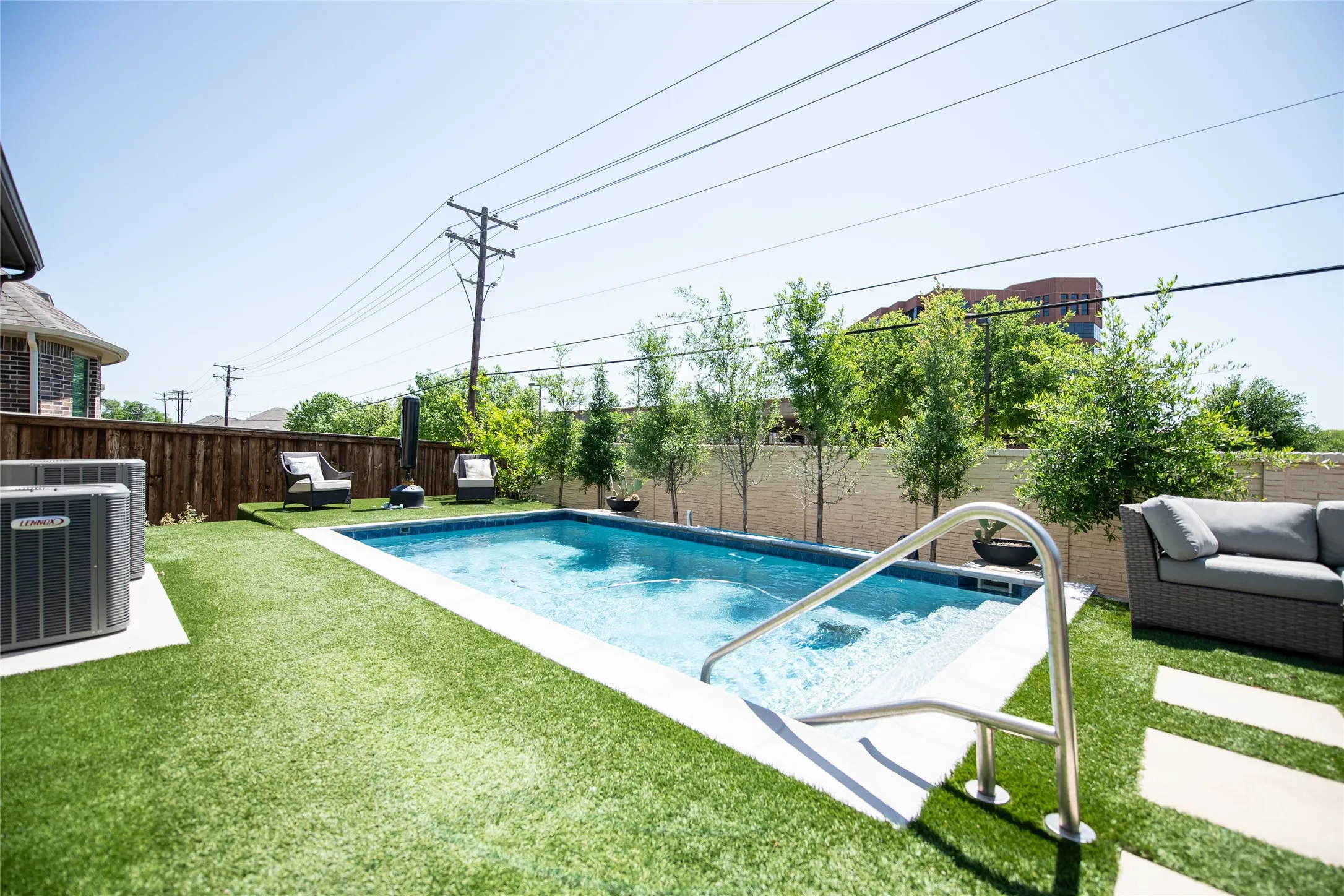 Private backyard featuring a rectangular swimming pool with integrated steps, artificial turf, and a stone privacy wall