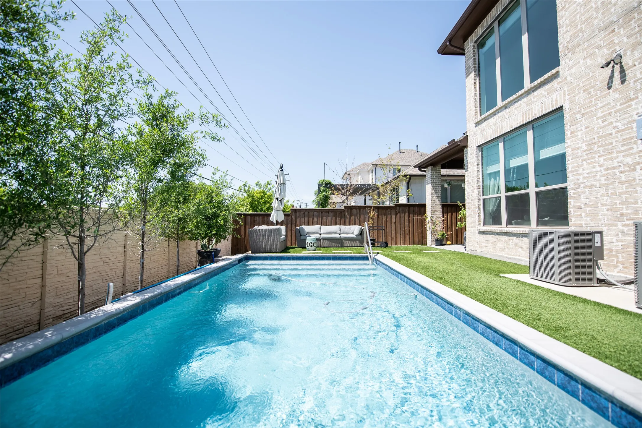 Rectangular swimming pool with integrated steps, surrounded by artificial turf and a brick-clad exterior
