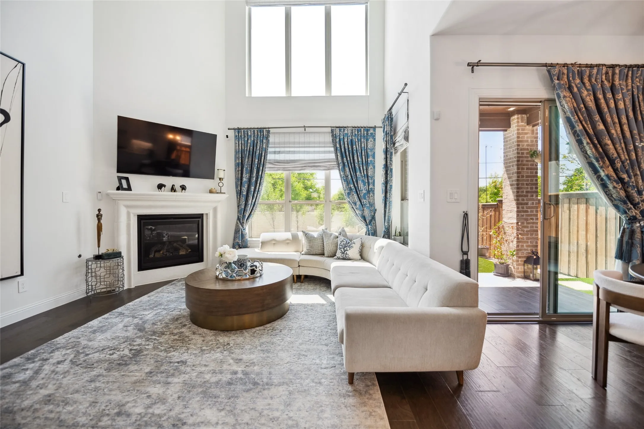 Vaulted ceiling with high windows, dark wood-finish flooring, built-in fireplace with mantel, large window with natural light, and sliding glass door