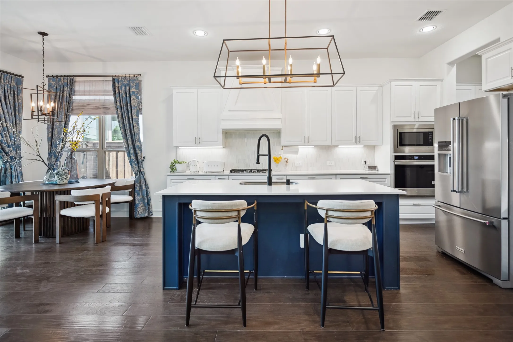 Kitchen featuring a central island with countertop seating, white cabinetry, integrated stainless steel appliances, and wood-finish flooring
