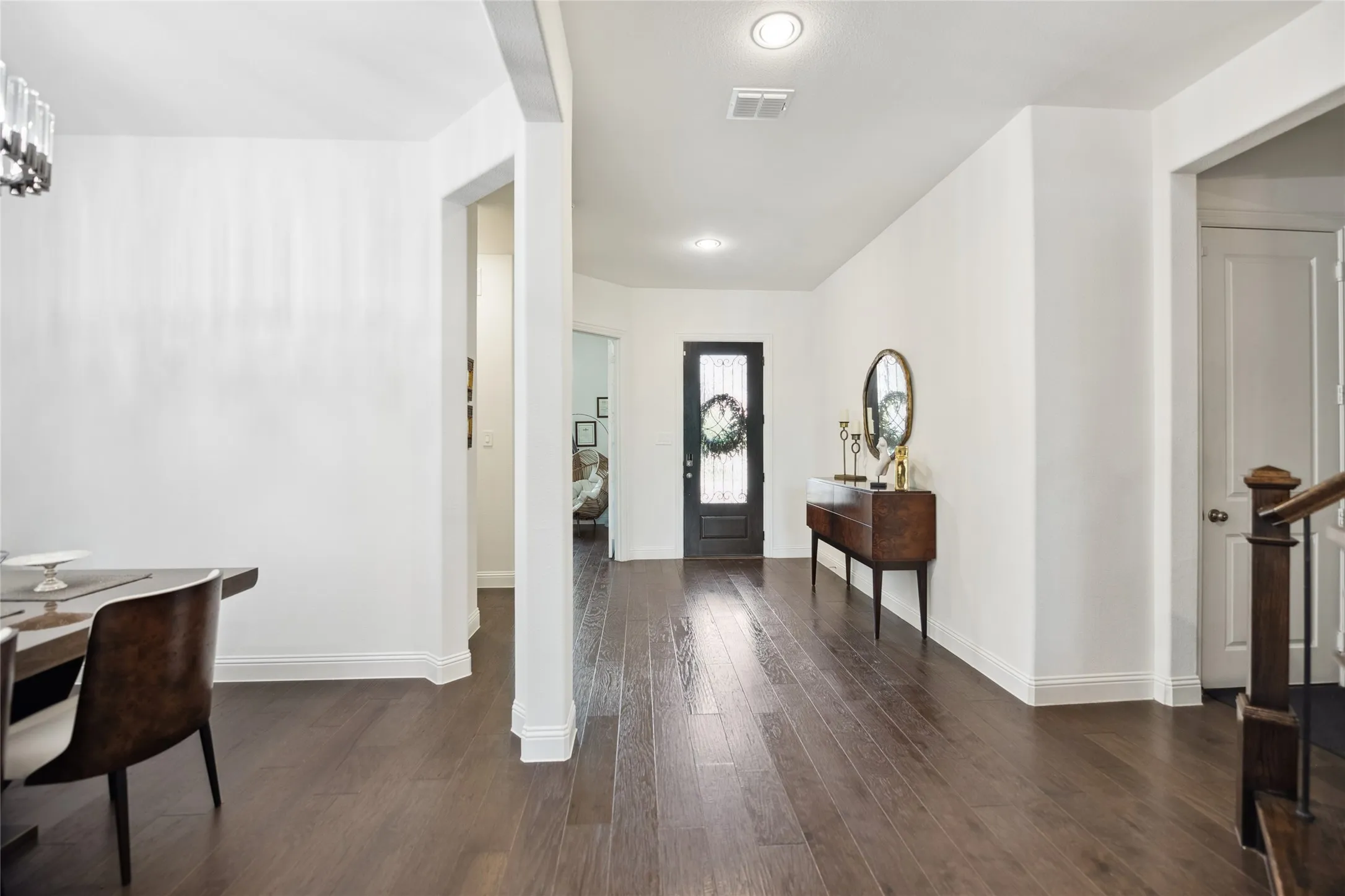 Hardwood-finish flooring, recessed ceiling lighting, a dark wood-finish front door with glass inserts, and a wood-finish staircase with dark wood newel posts