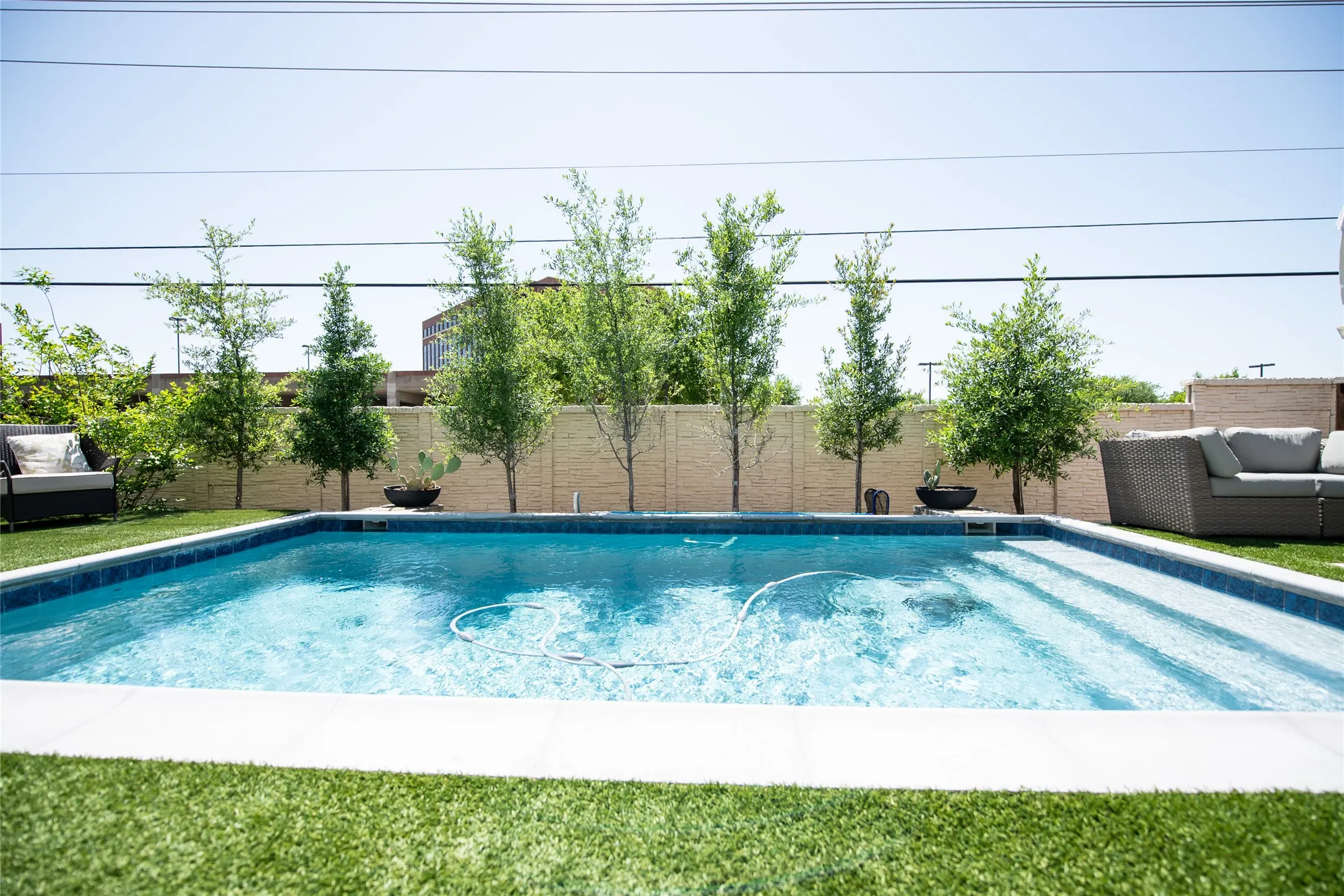 Rectangular inground swimming pool with integrated steps, surrounded by artificial turf and a perimeter wall
