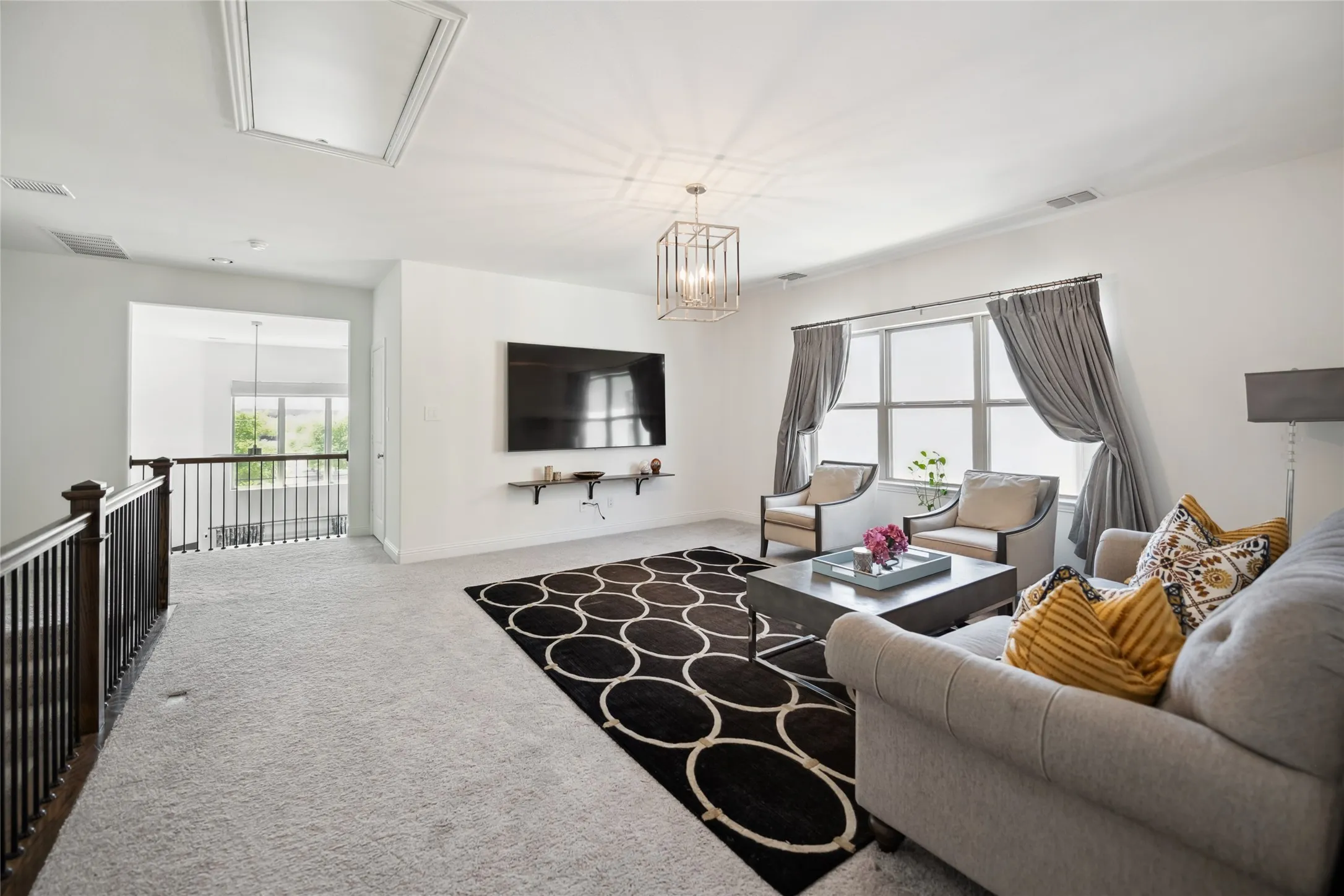 Carpeted living area featuring a decorative chandelier, large window, and dark wood railing