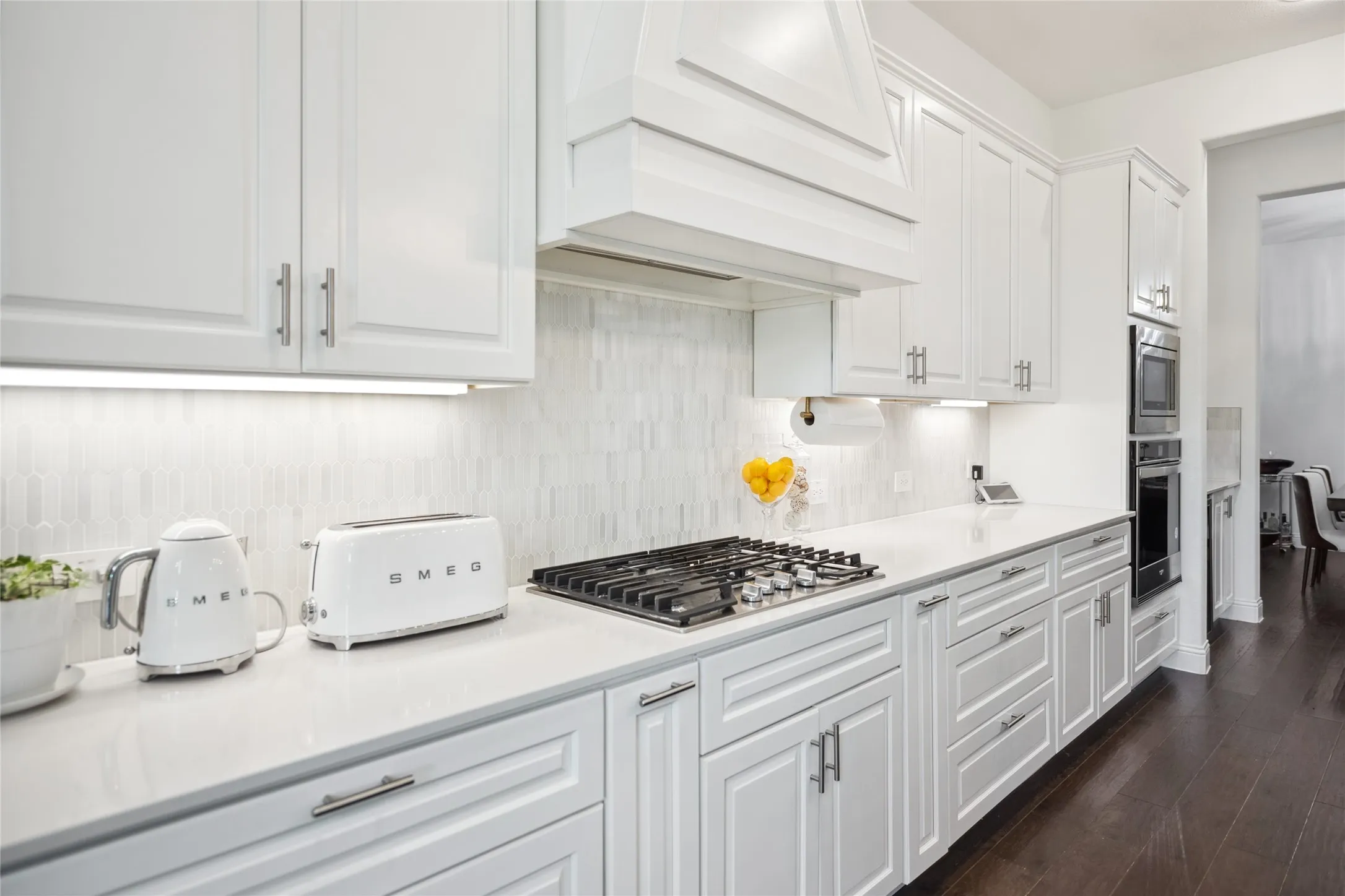 White shaker-style cabinetry with satin nickel hardware, a gas cooktop, built-in double ovens, and light-toned tile backsplash