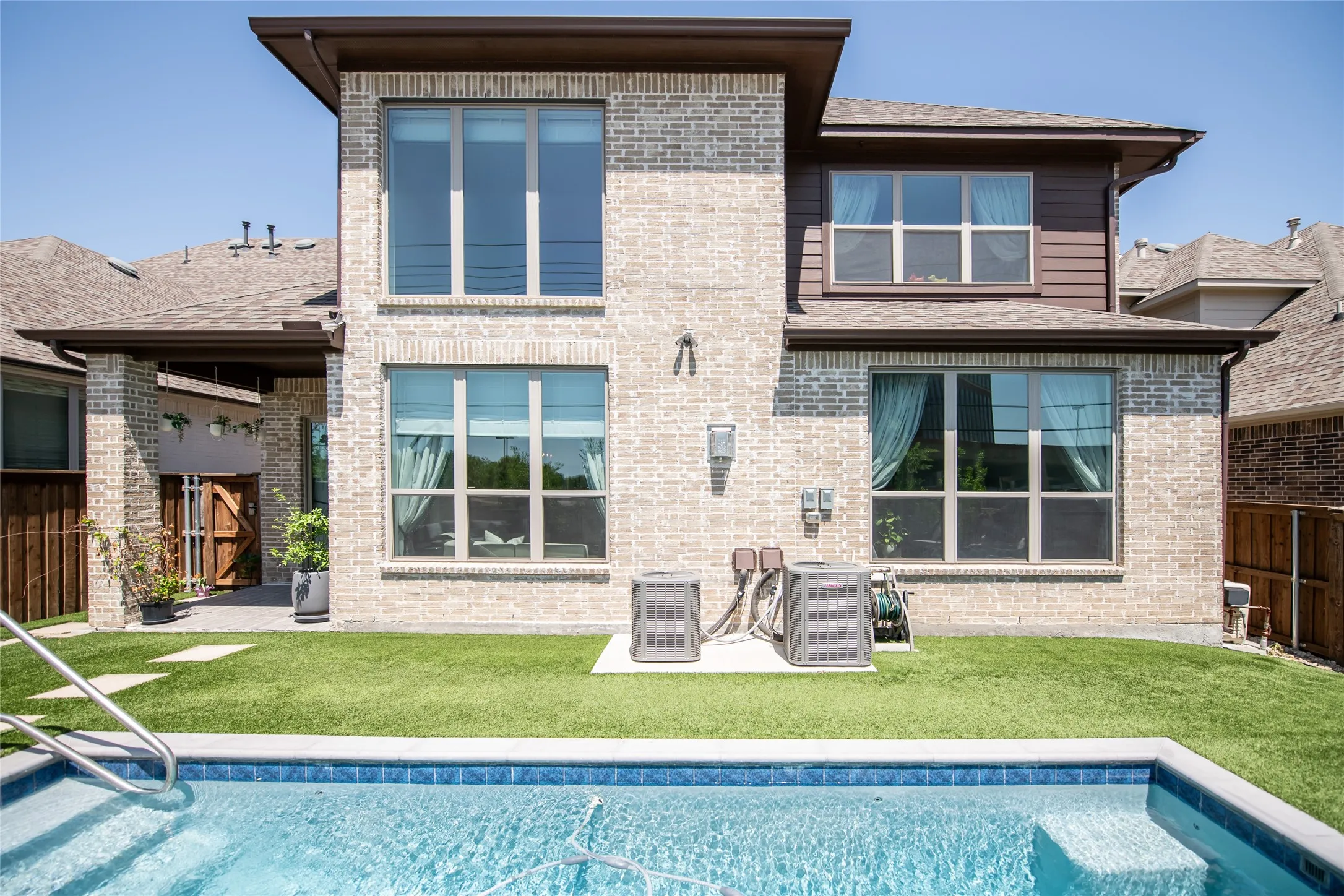 Brick exterior with integrated wood siding accents, a sparkling blue-tiled swimming pool, artificial turf, and a covered patio with a wood-paneled door