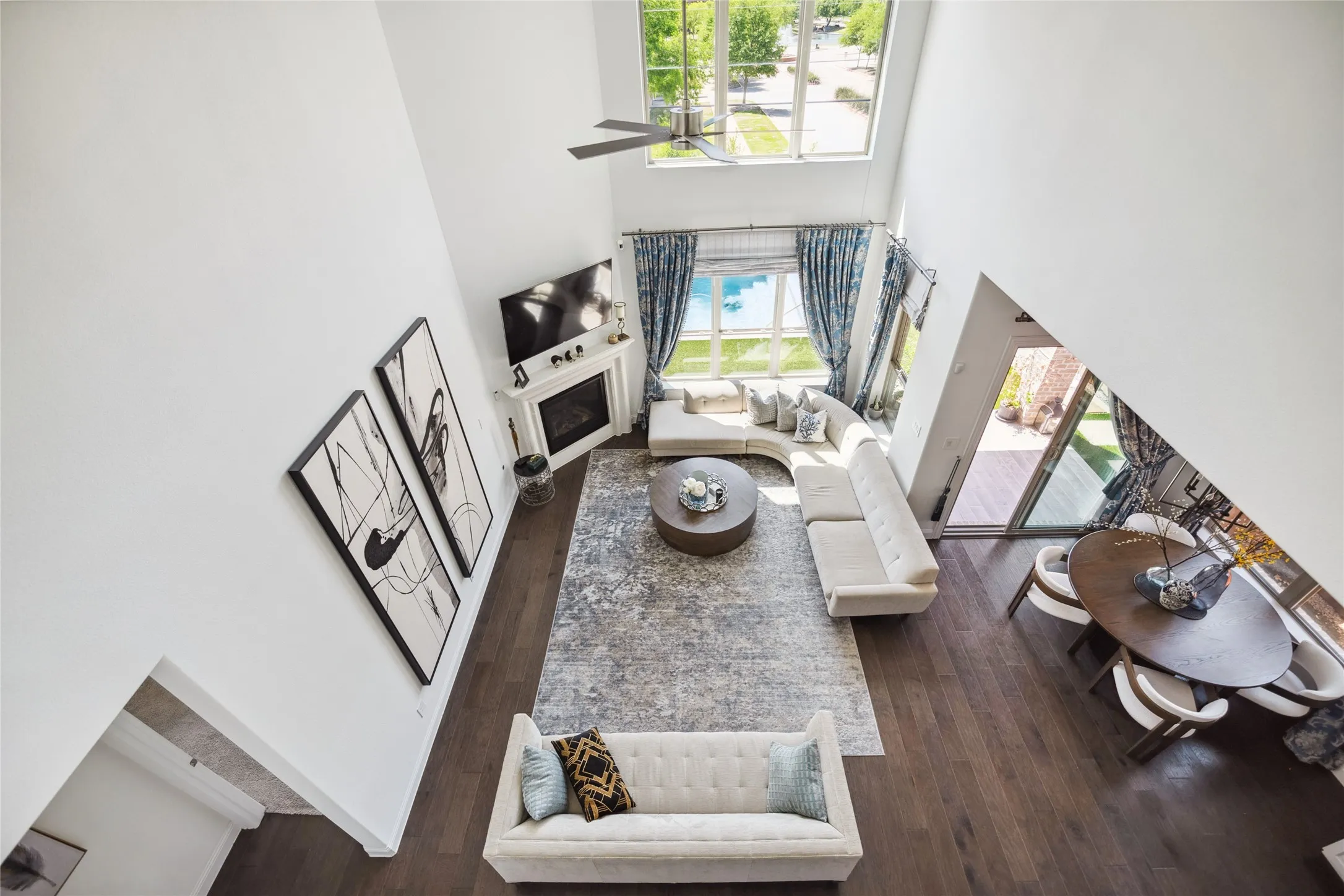 Two-story living area with dark wood-finish flooring, a white mantel fireplace, and a ceiling fan