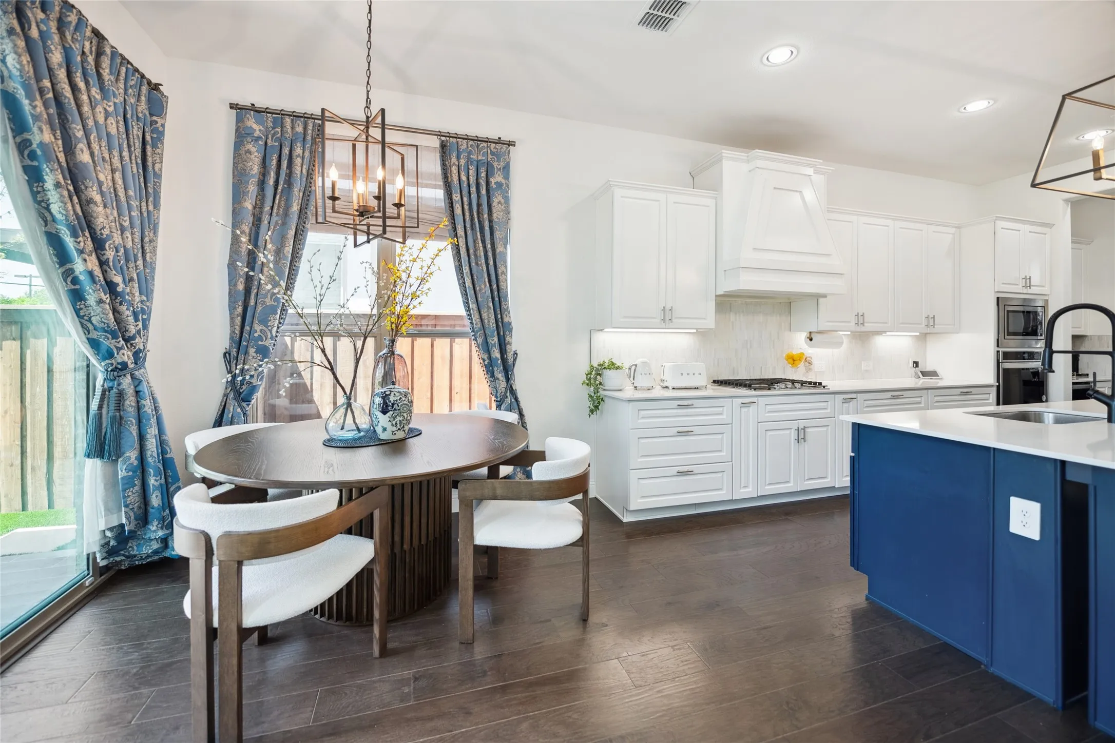Kitchen featuring wood-finish flooring, white cabinetry, a built-in gas range, and a blue island with an integrated sink