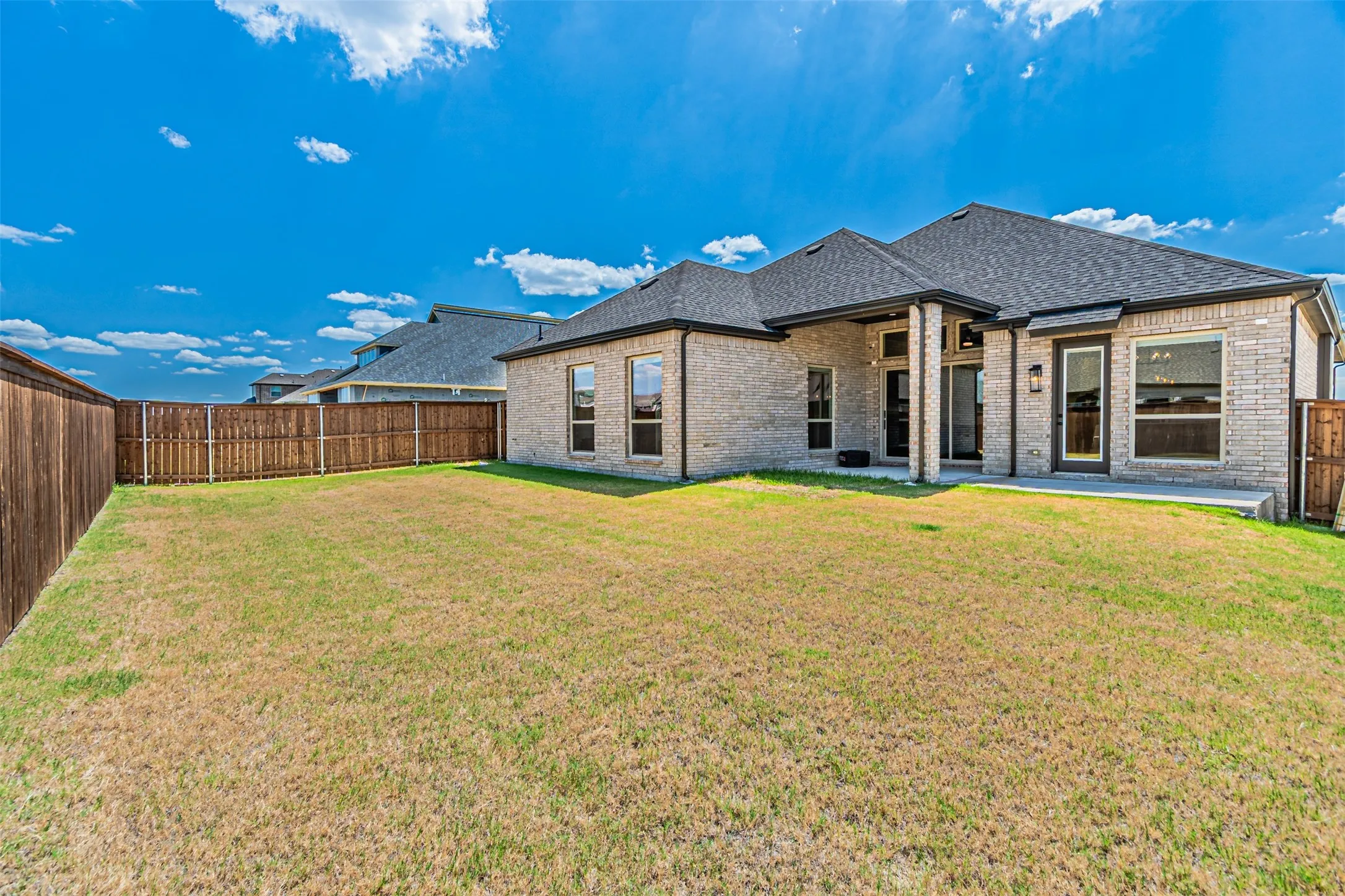 Expansive backyard featuring a brick exterior, covered patio, and wood privacy fencing