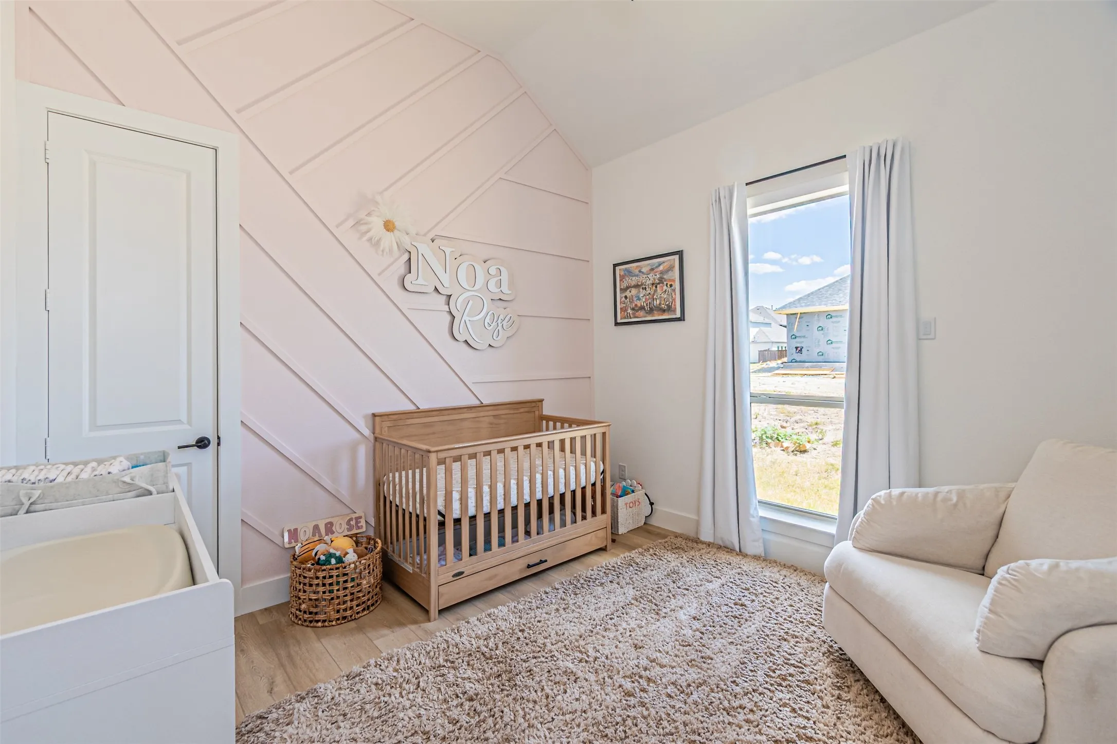 Vaulted ceiling with shiplap accent wall, white interior door with black hardware, wood-finish flooring, and a large window