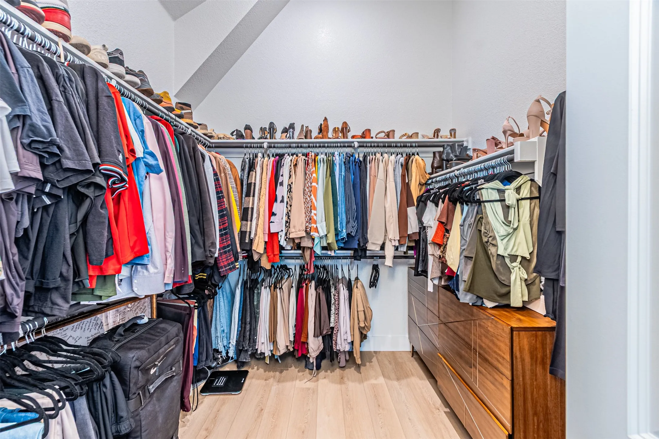 Walk-in closet featuring wood-finish flooring, built-in shelving, multiple hanging rods, and an integrated wood-finish dresser