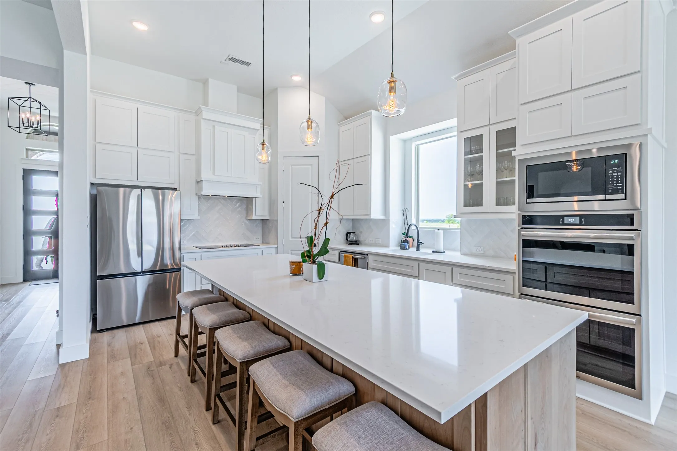 Gourmet kitchen featuring a large central island, stainless steel appliances, white cabinetry, and wood-finish flooring