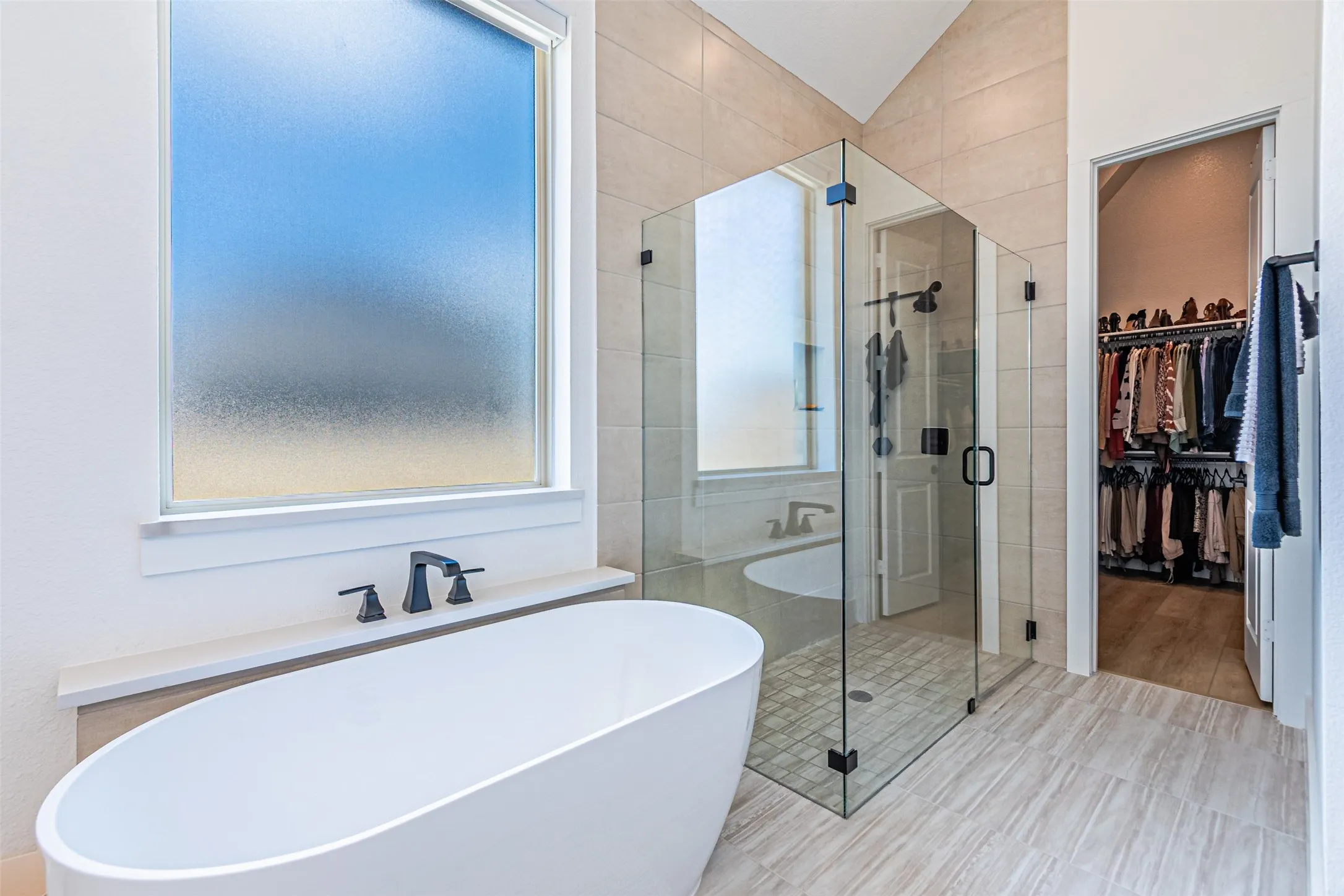 Freestanding soaking tub with matte black fixtures, glass-enclosed shower, tiled flooring, and vaulted ceiling