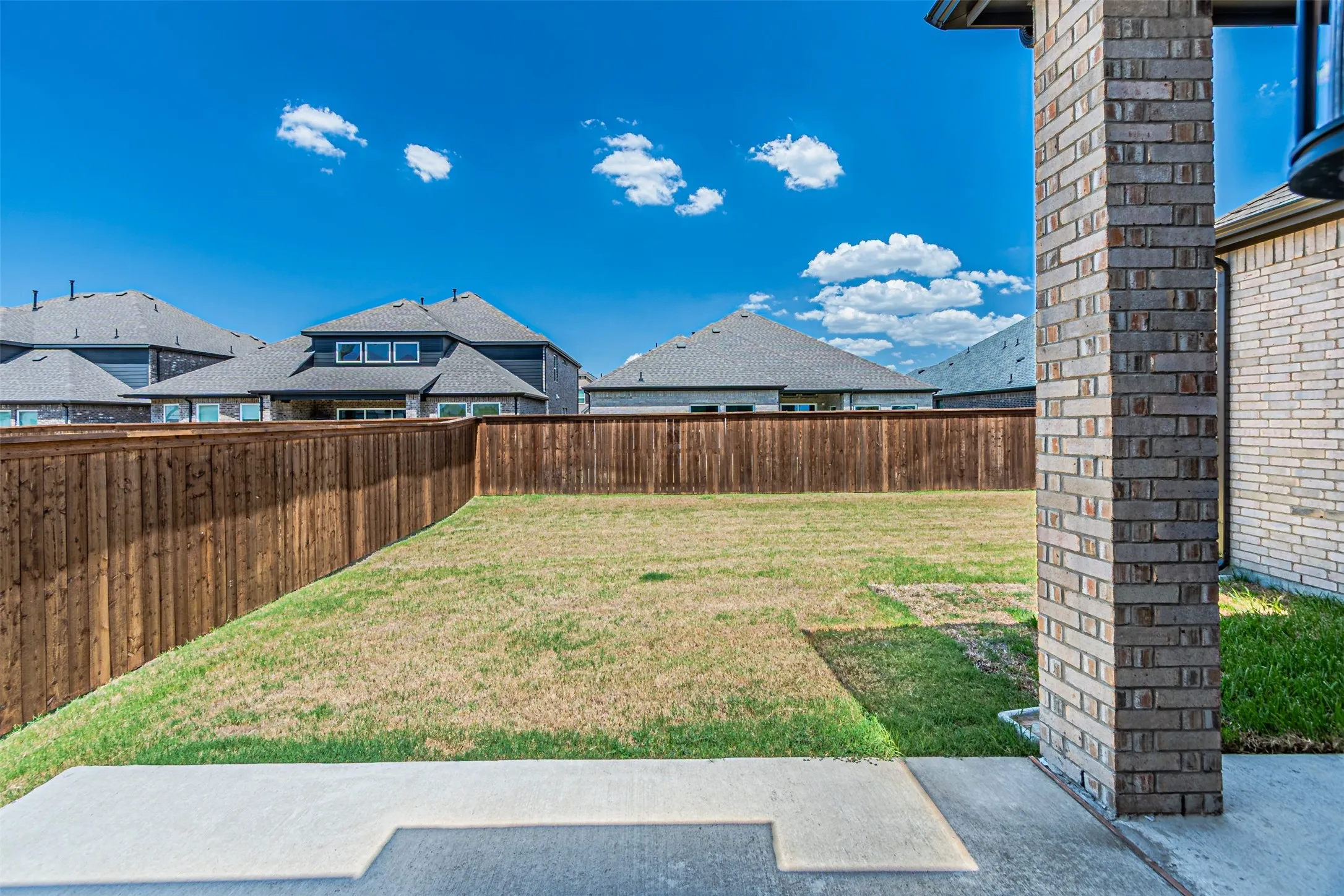 Expansive backyard with a wooden fence, concrete patio, and brick column