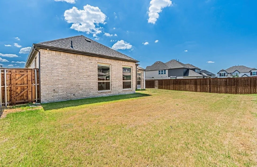 Expansive backyard featuring a privacy fence, brick exterior, multiple windows, and a dark shingle roof