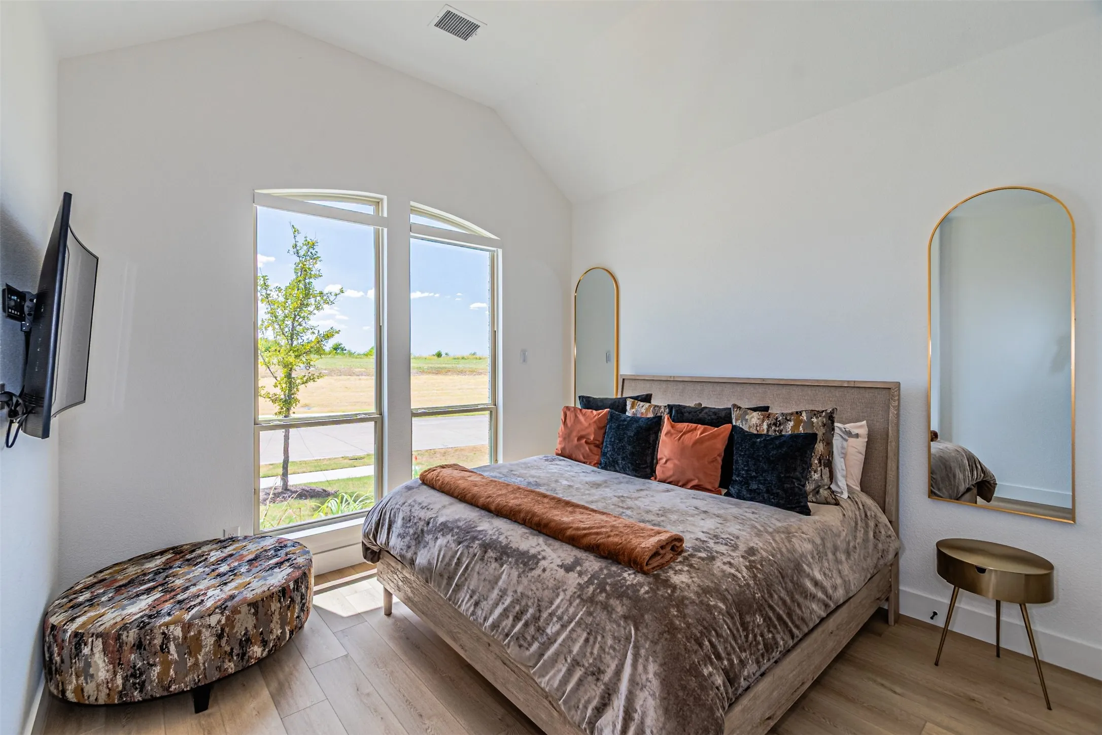 Vaulted ceiling with wood-finish flooring, featuring a large arched window