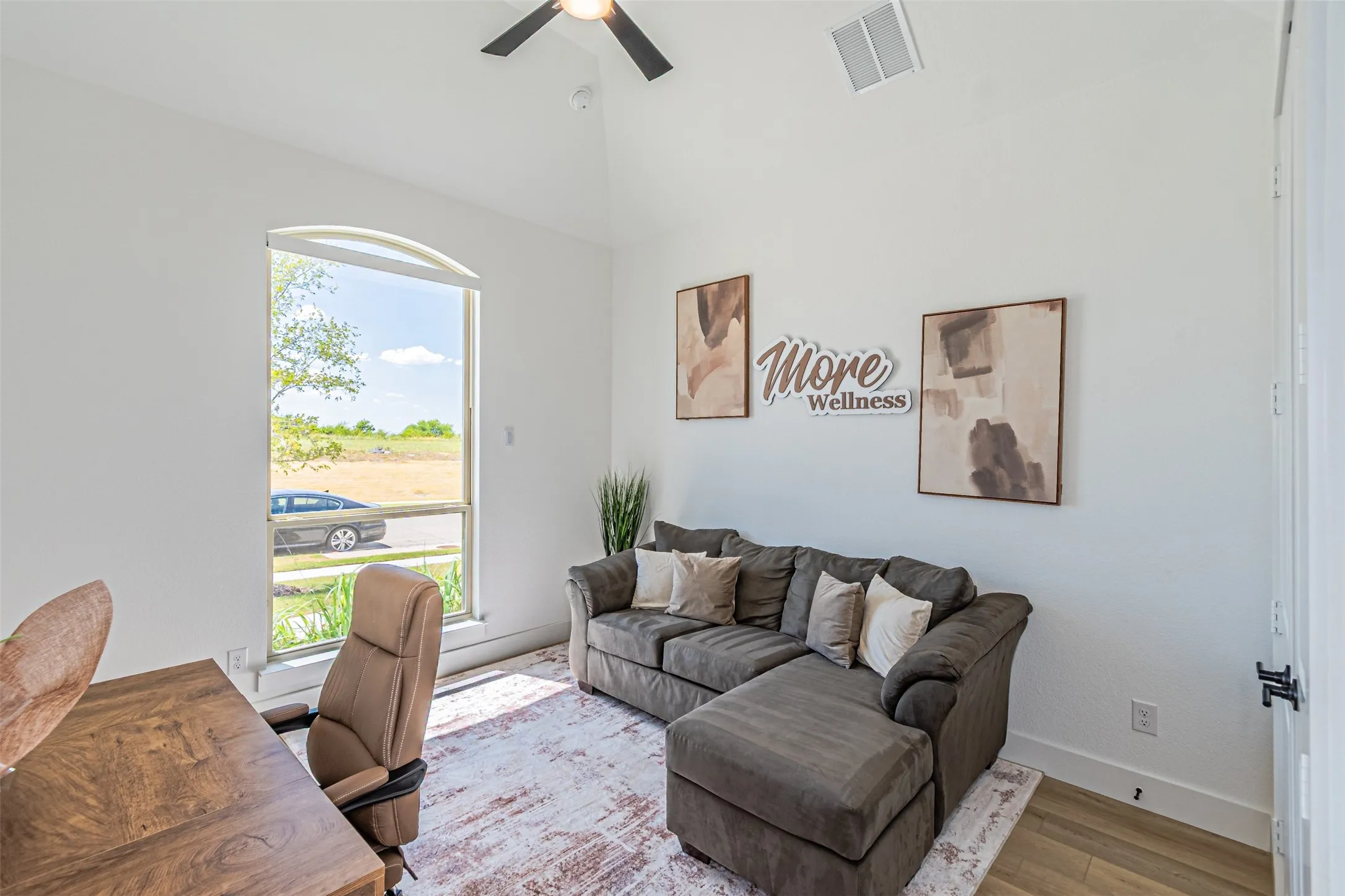 Arched window, vaulted ceiling, ceiling fan, wood-finish flooring, white walls