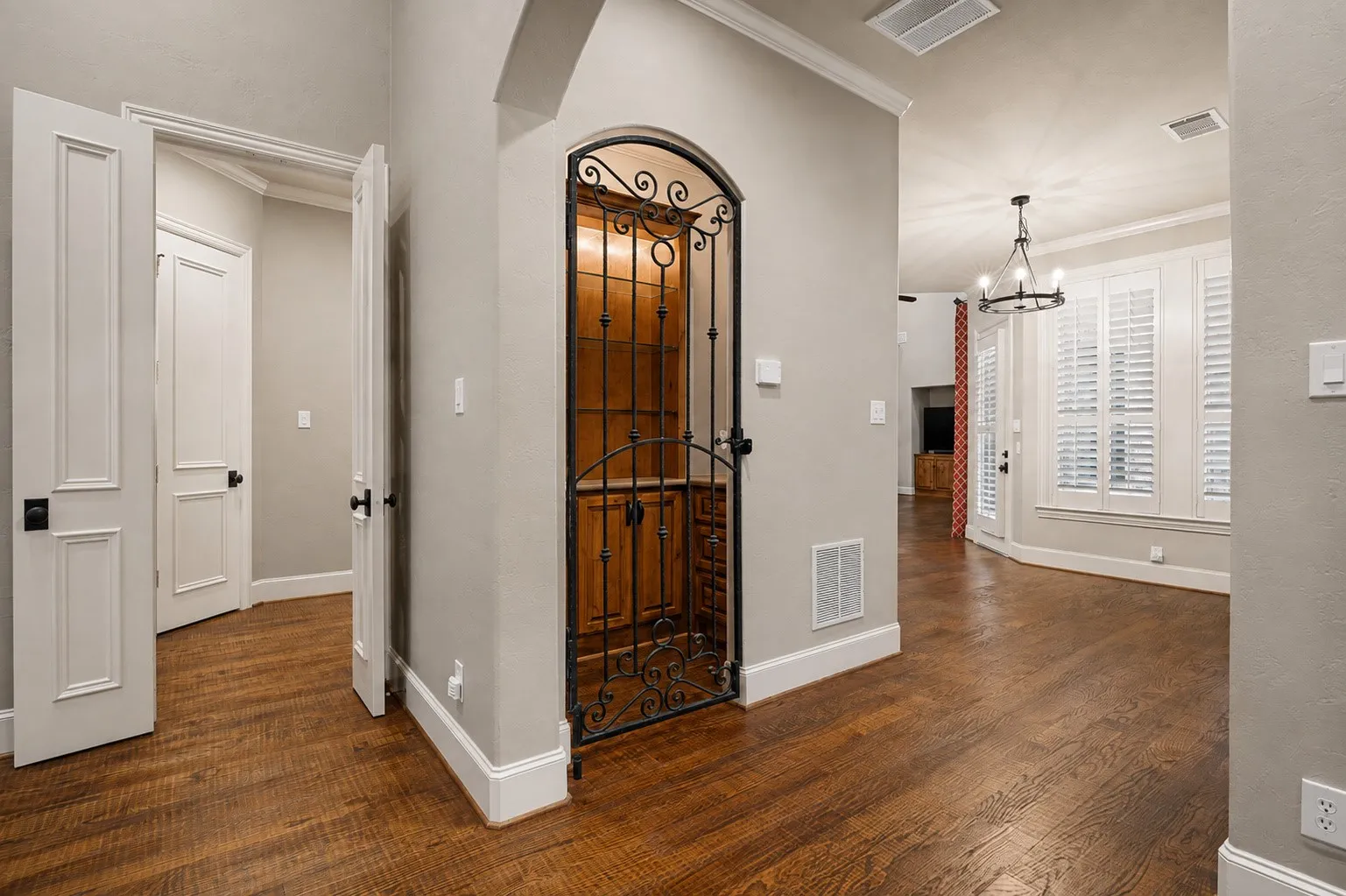 Wood-finish flooring, white trim, arched doorway, wrought iron gate, and ceiling-mounted chandelier
