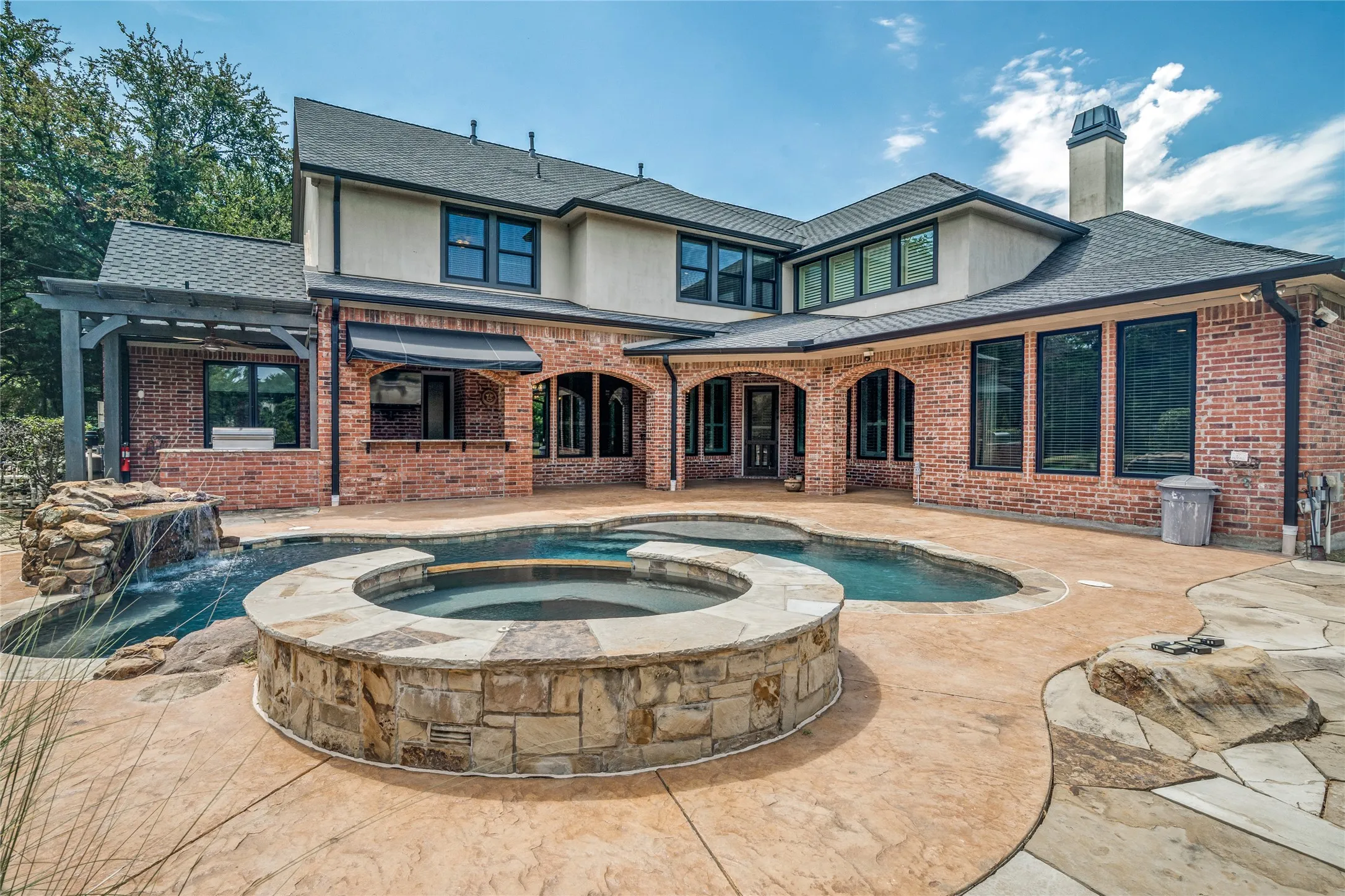 Spacious backyard featuring a custom-shaped swimming pool, integrated spa, stone waterfall, and expansive stamped concrete patio