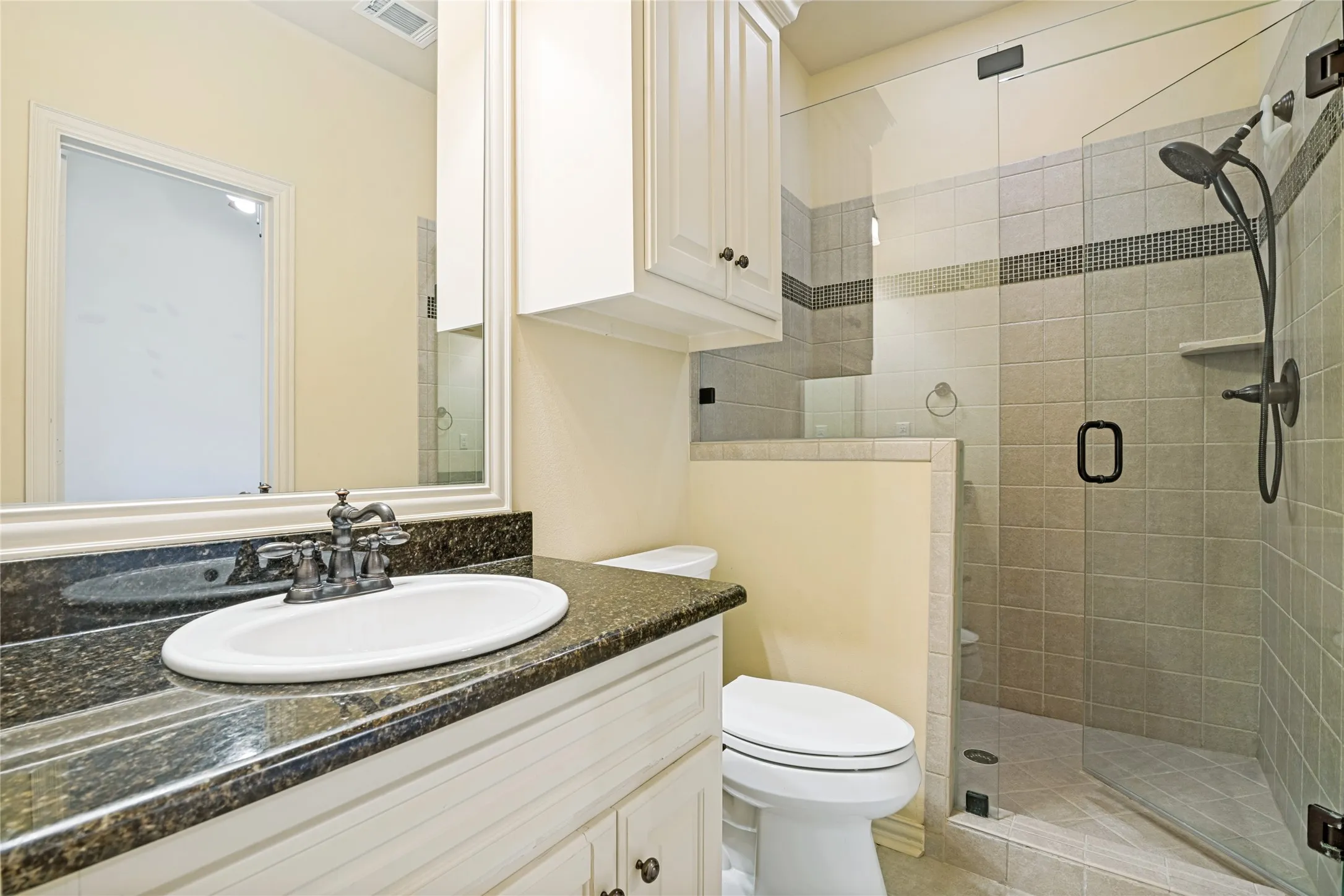 Frameless glass shower enclosure with tiled walls, dark-finish shower fixtures, and a corner shelf