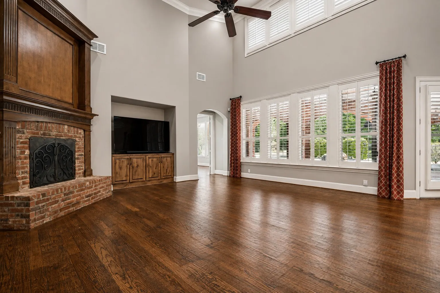 Two-story ceiling, wood-finish flooring, brick fireplace with wood mantel, built-in media cabinet, and plantation shutters