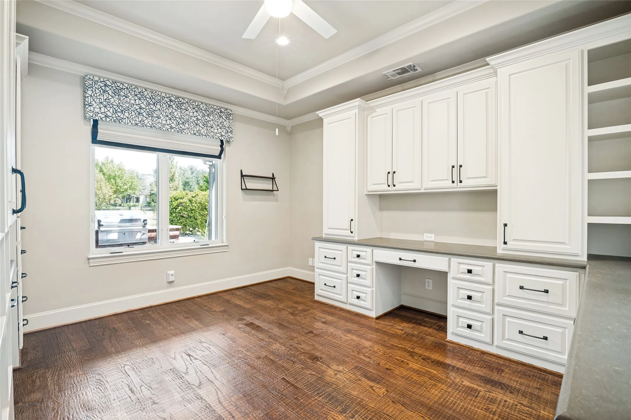 Bright home office featuring extensive white cabinetry with brushed metal hardware, a spacious work surface with multiple storage drawers, and wood-finish flooring