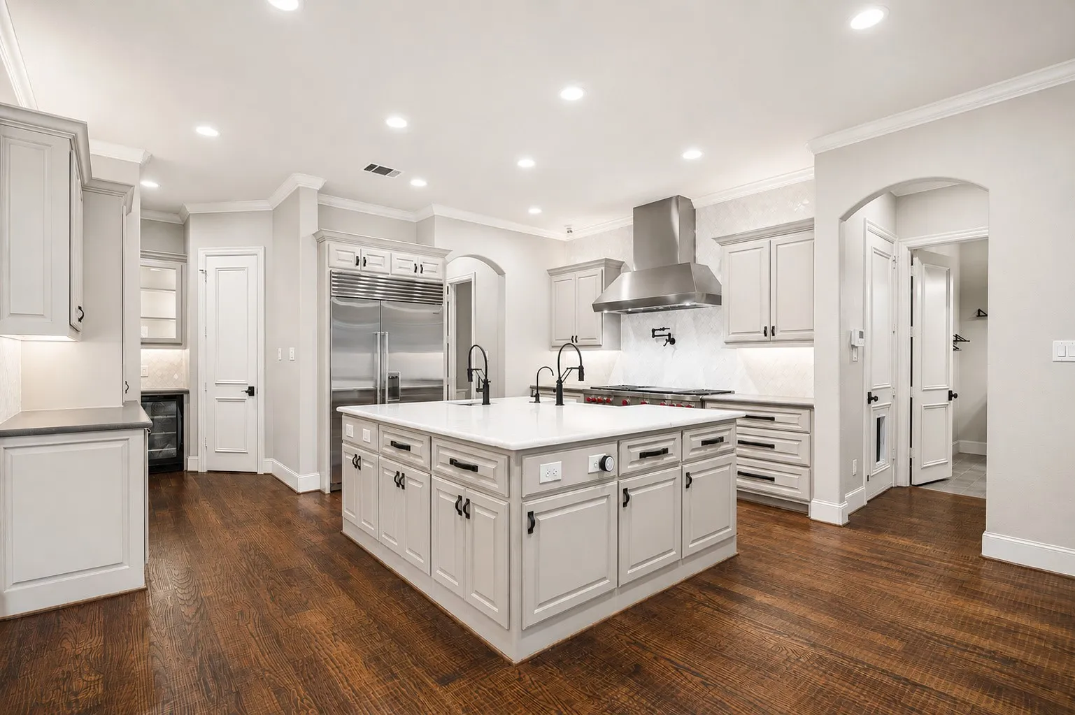 Gourmet kitchen featuring a large central island, white cabinetry, stainless steel appliances, and dark wood-finish flooring