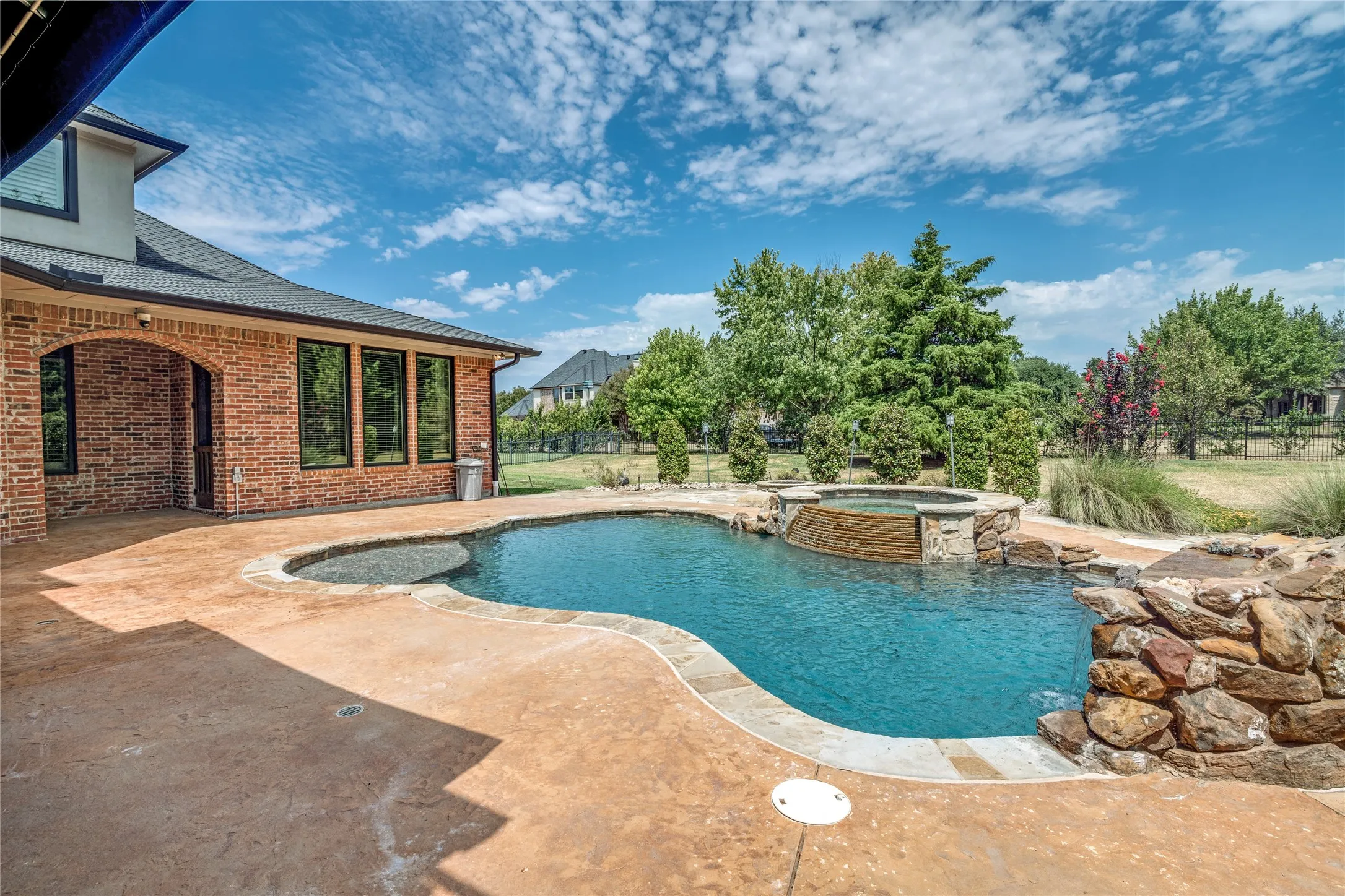 Expansive stamped concrete patio with an irregular-shaped pool, integrated spa, and rock waterfall feature