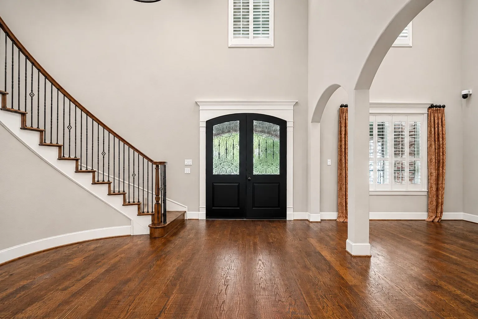 Hardwood flooring, curved staircase with wrought iron balusters, double entry doors, arched doorways, and tall windows with plantation shutters