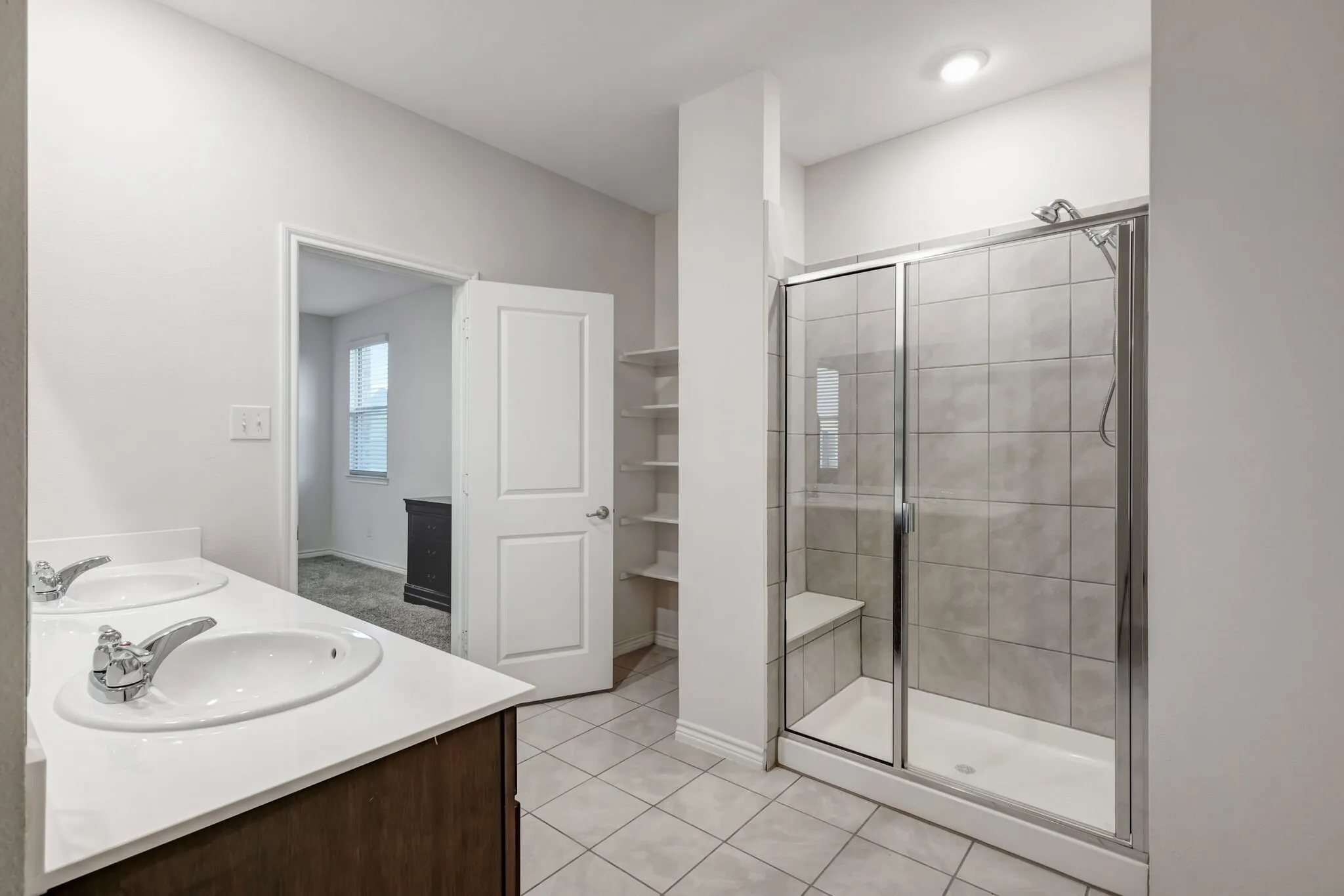 Dual sink vanity with white countertop, walk-in shower with tiled walls and built-in bench, and tiled flooring