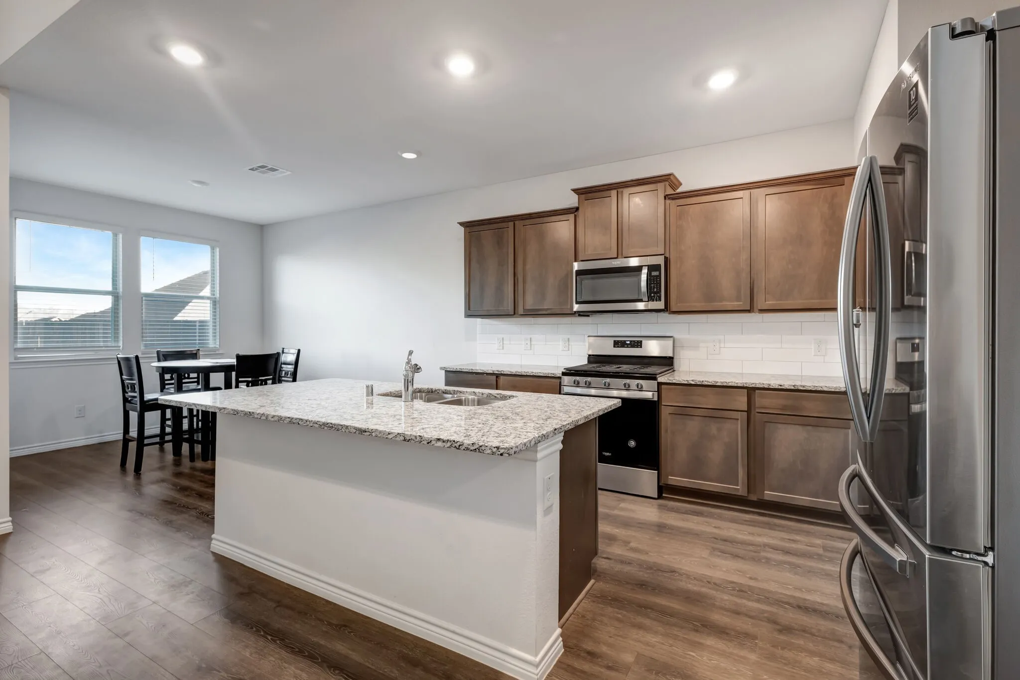 Kitchen featuring wood-finish flooring, recessed lighting, and a center island with a sink and stone countertop
