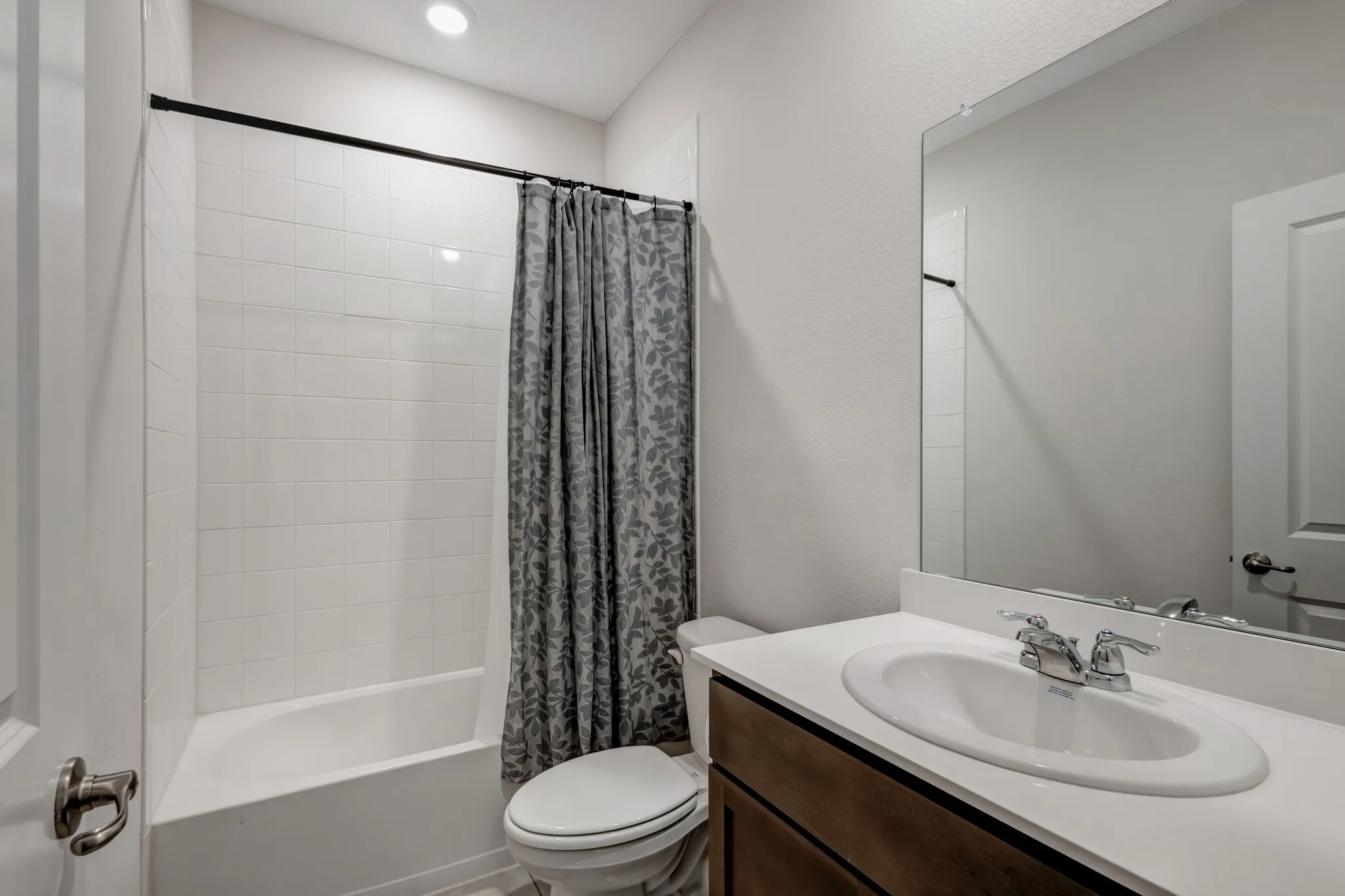 Bathroom featuring a built-in tub with tile surround, a single vanity with a white countertop, an undermount sink, and a wall-mounted mirror