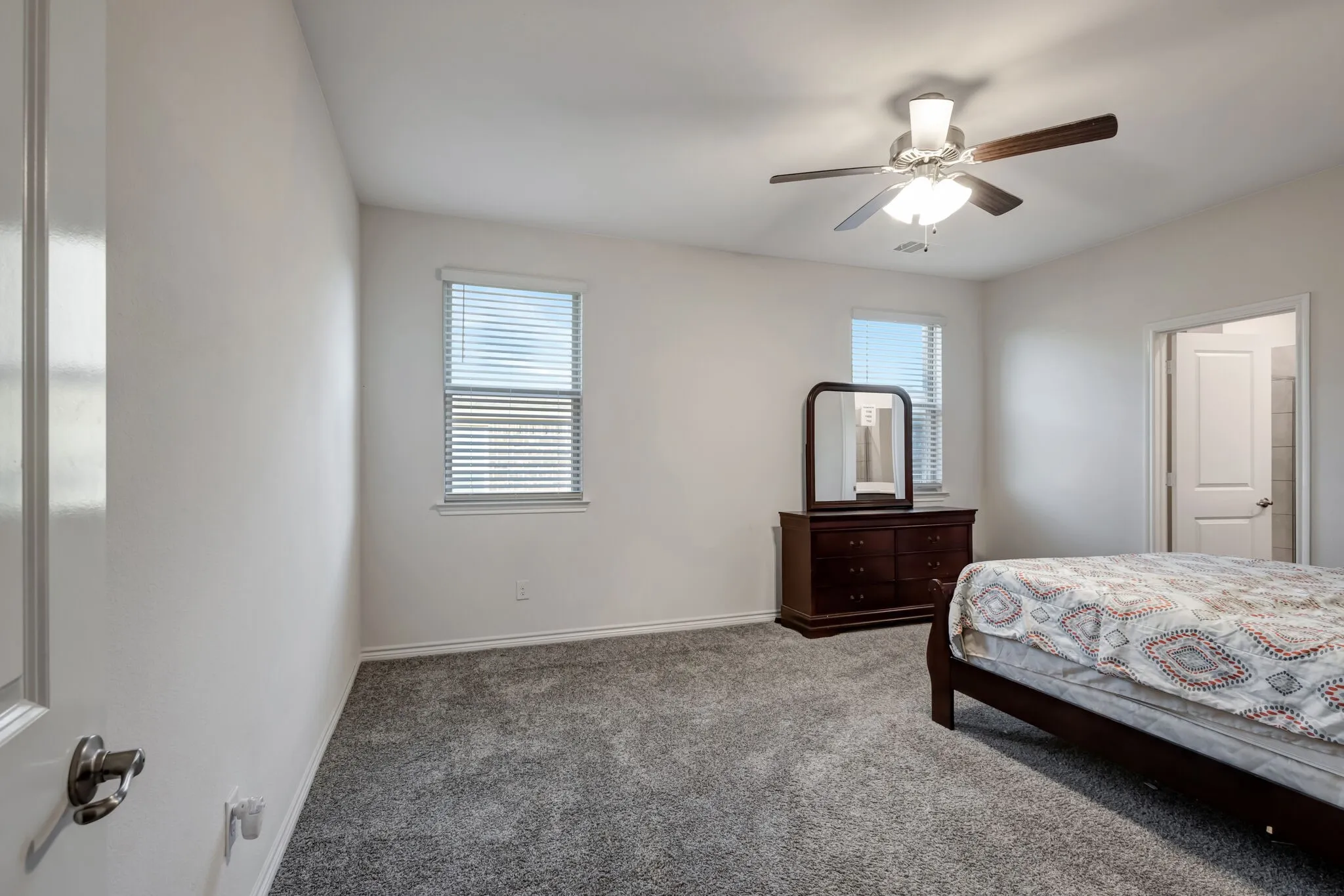 Neutral wall color, gray carpeting, dual windows with blinds, ceiling fan with integrated lighting, and a white interior door