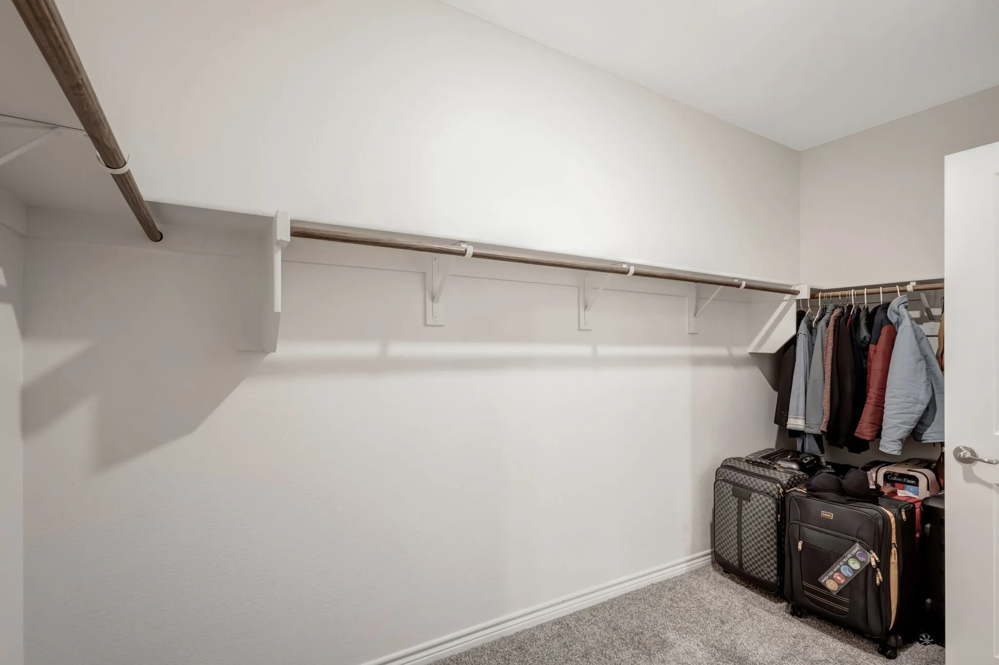 Walk-in closet featuring white walls, wood-finish hanging rods, and gray carpeting