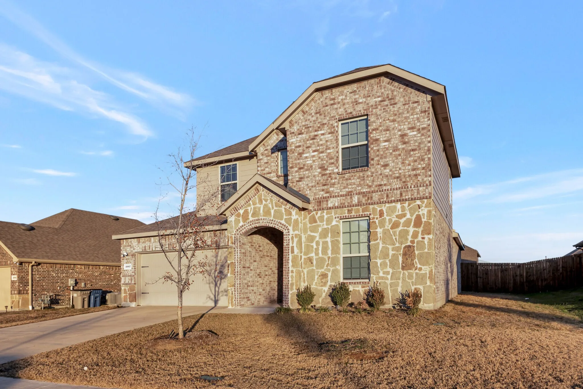 Two-story residence featuring a mixed-material exterior, arched entry, attached garage, and a fenced yard