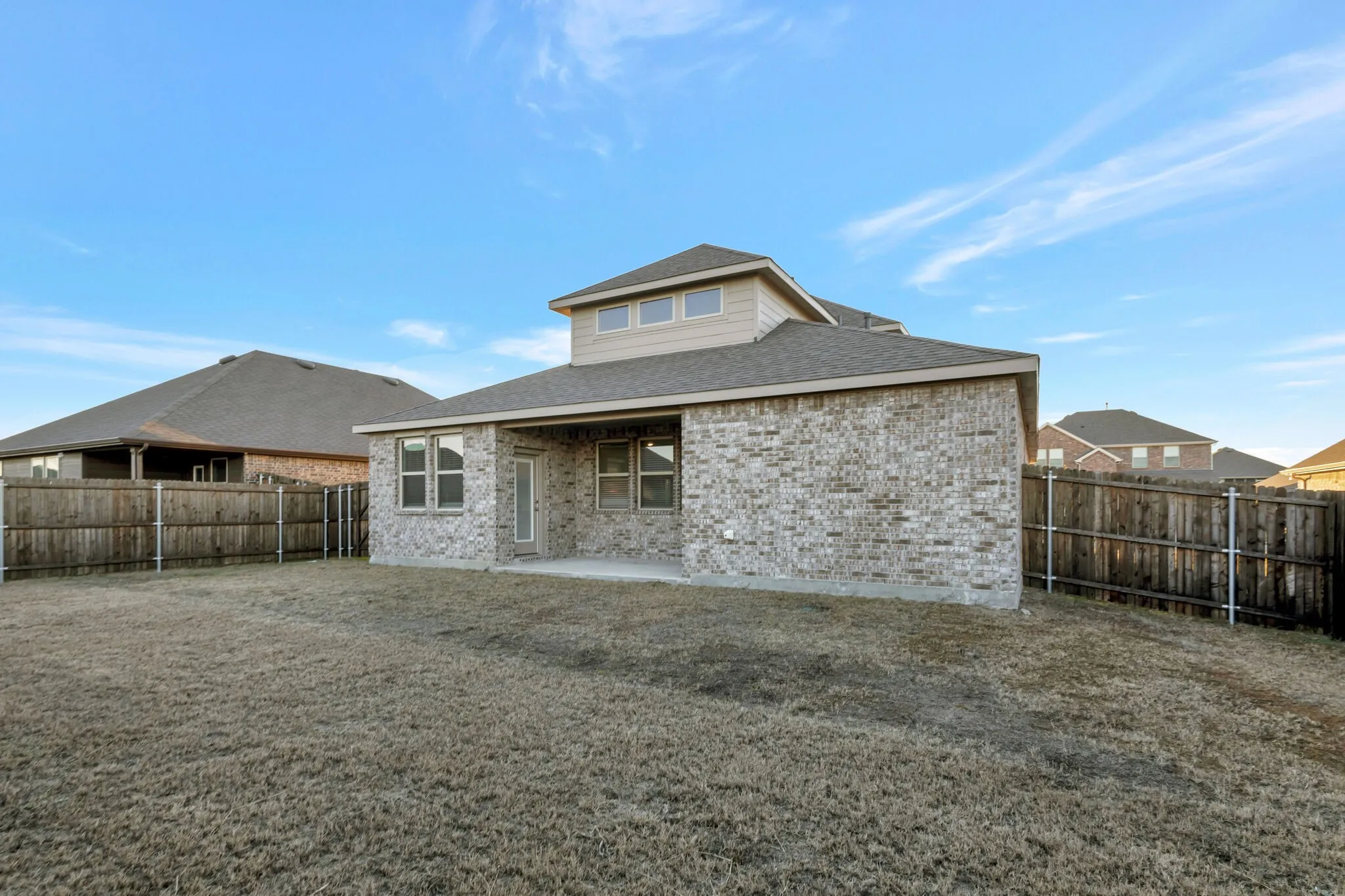 Rear exterior featuring a brick facade, covered patio, multiple windows, and a fully fenced yard