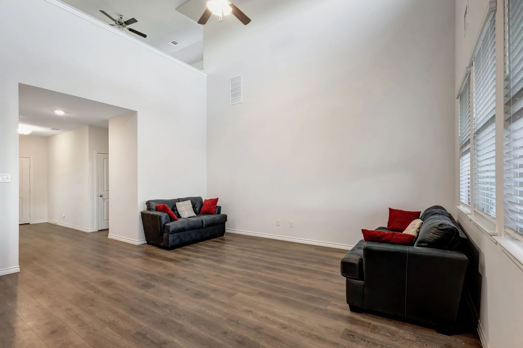 Vaulted ceiling with ceiling fan, wood-finish flooring, multiple windows with blinds, and white trim throughout